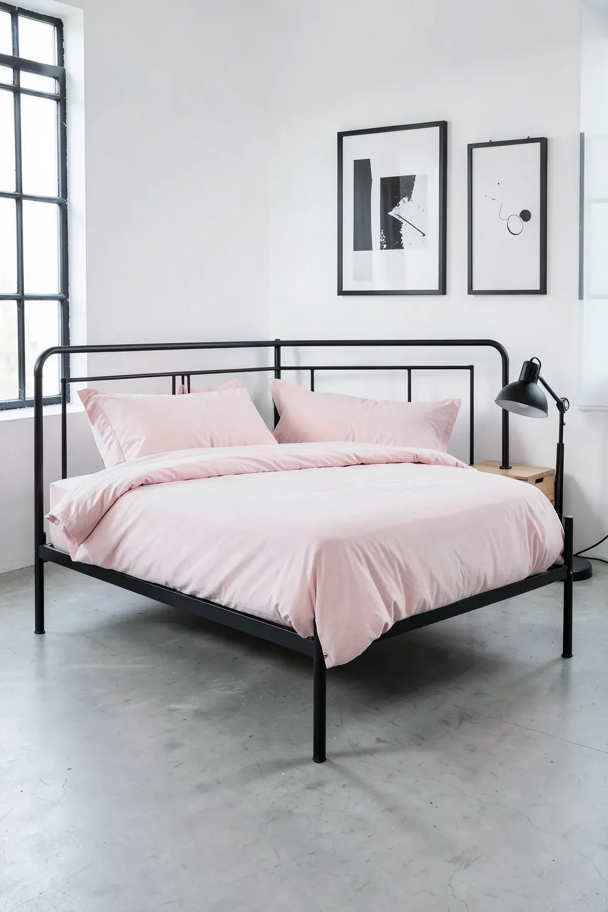 A modern bedroom with a matte black metal bed frame and soft pastel pink bedding against white walls.