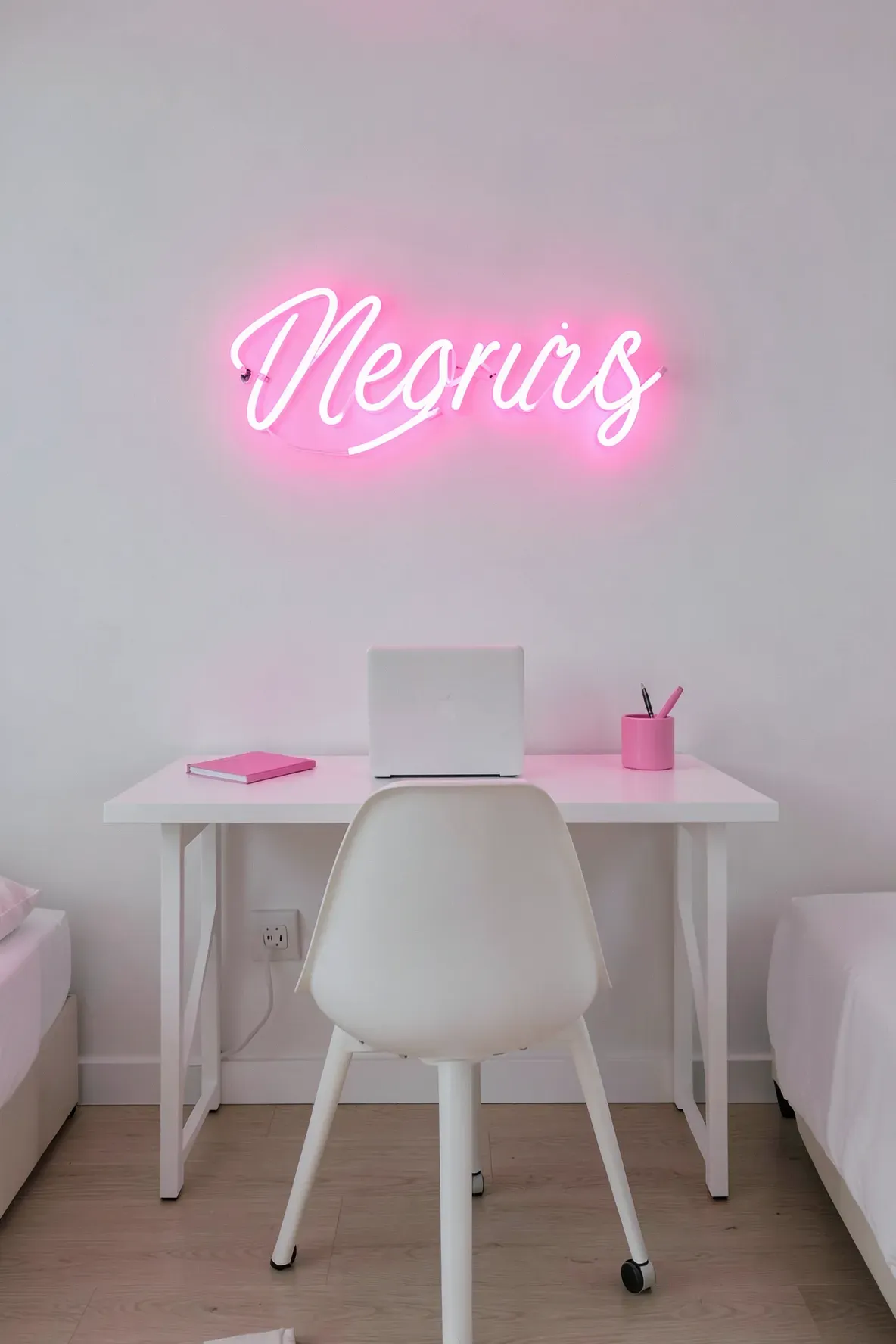 A modern bedroom workspace with a glowing hot pink neon sign hanging above a minimalist white desk.
