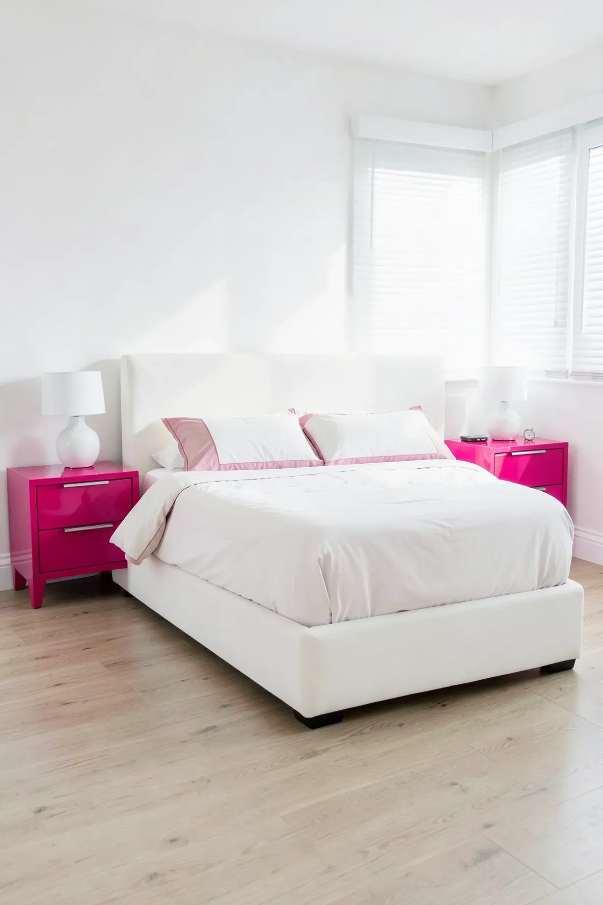Symmetrical glossy hot pink nightstands flanking a white bed in a sunlit room.