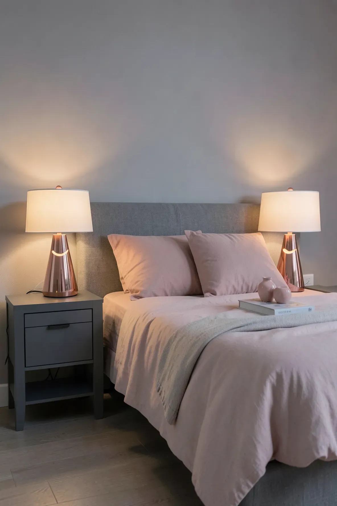 Rose gold lamps on slate grey bedside tables in a modern pink and grey bedroom.