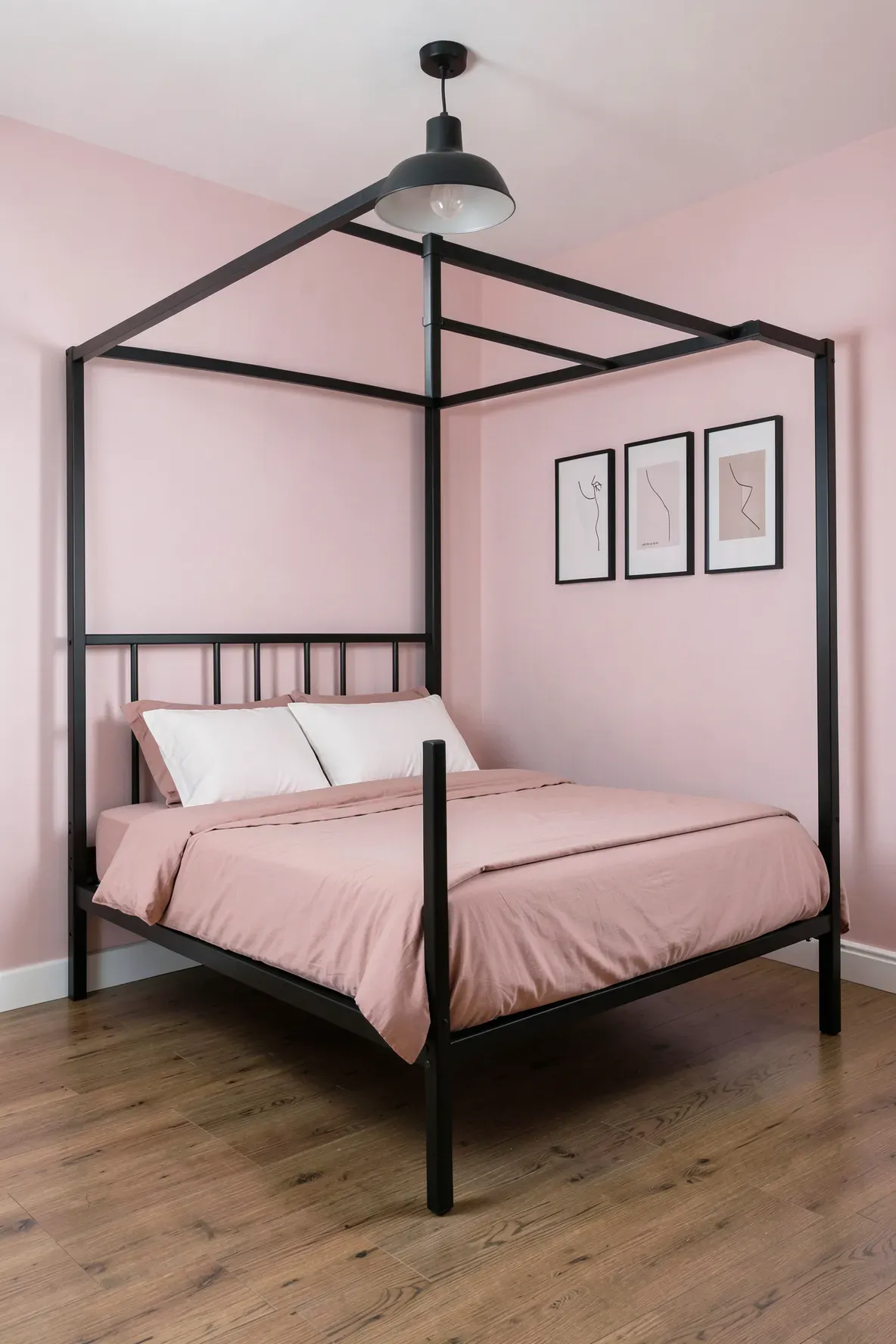A matte black metal bed frame creates a sharp contrast against pale pink walls in a modern bedroom.