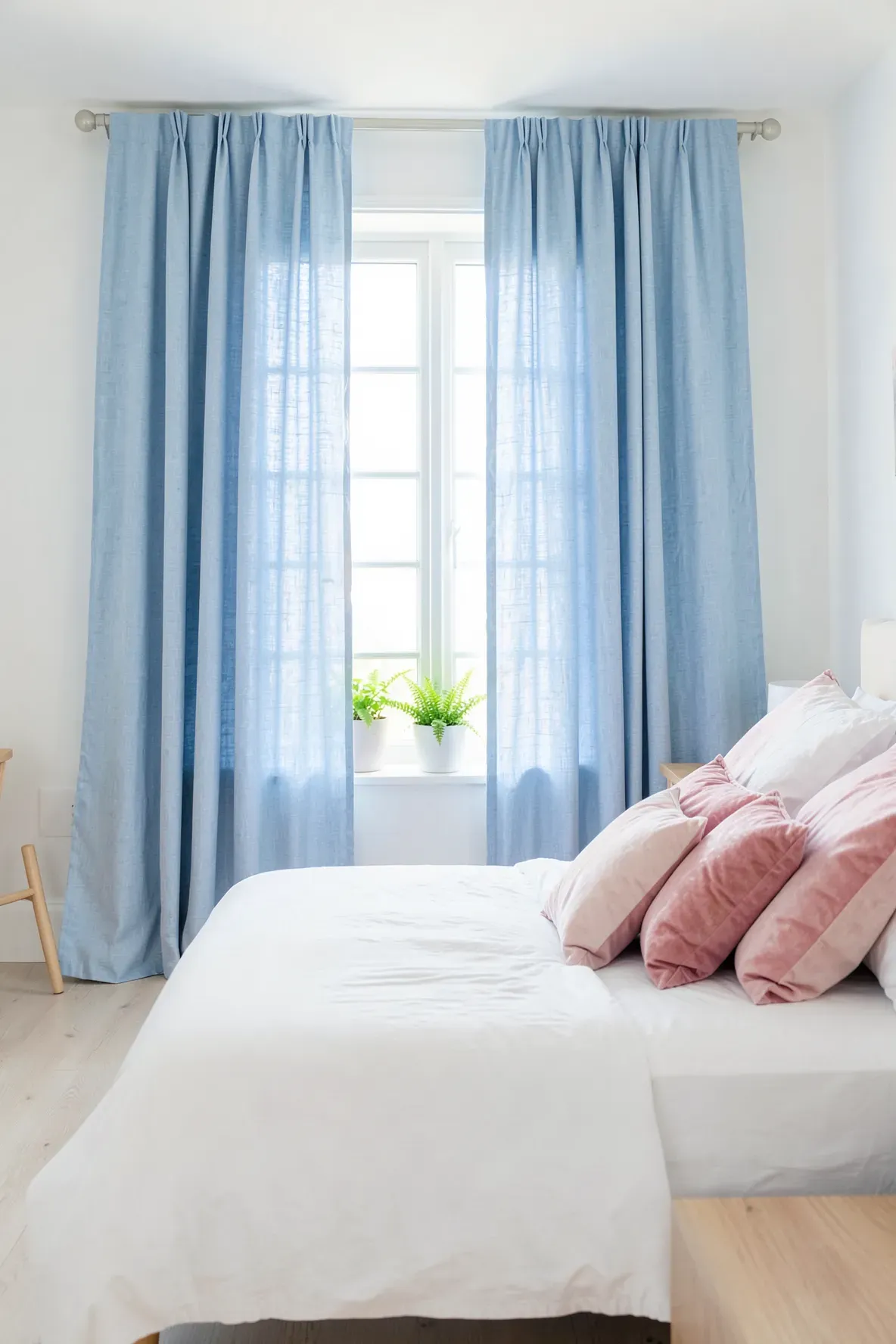 A bright bedroom featuring sky blue curtains framing a window behind a bed with pink pillows.