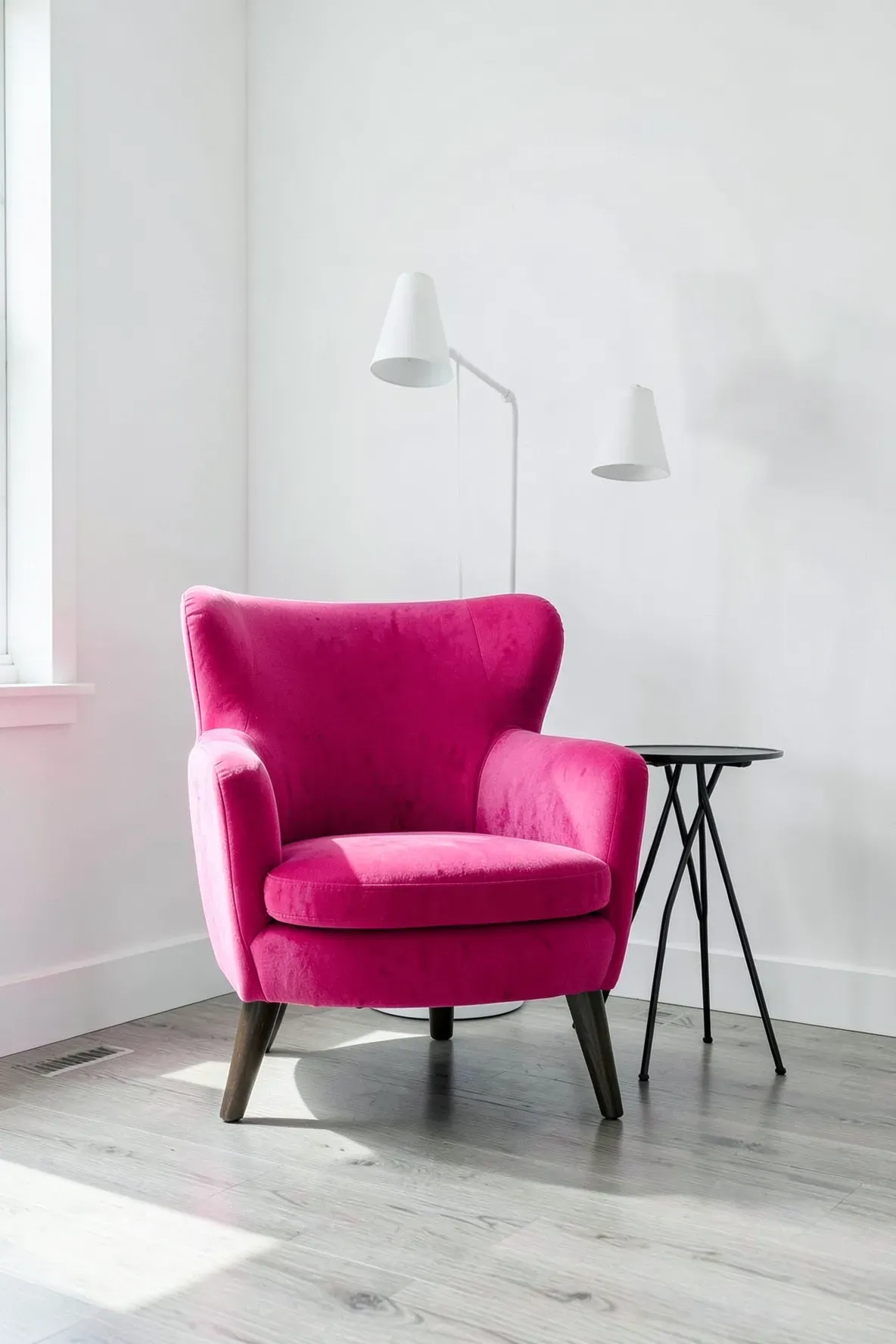A bold hot pink velvet accent chair standing against a plain white wall in a modern bedroom.
