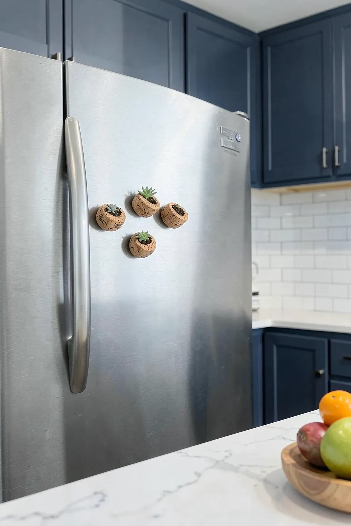 Small wine corks used as magnets on a stainless steel fridge, each holding a tiny baby succulent.
