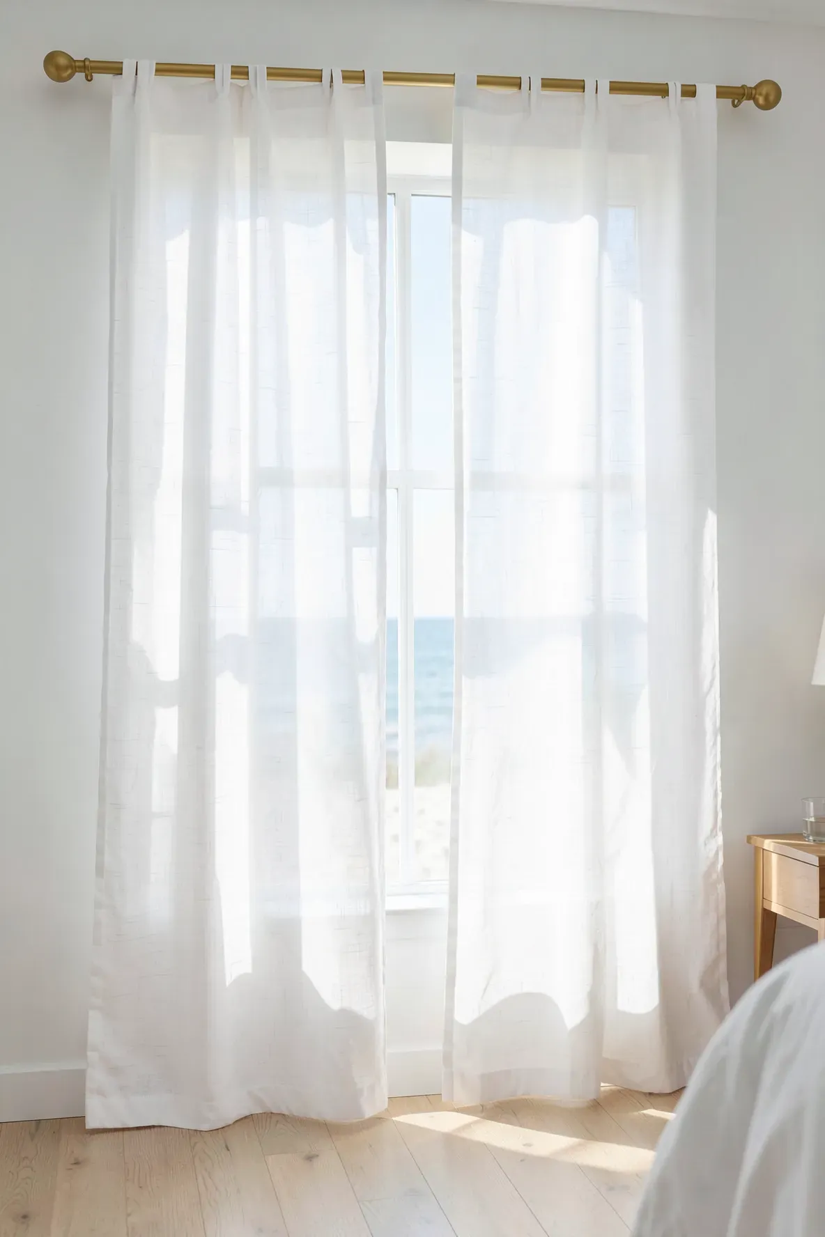 Sheer white curtains blowing in the breeze of a bright, sun-drenched beach vibe bedroom.