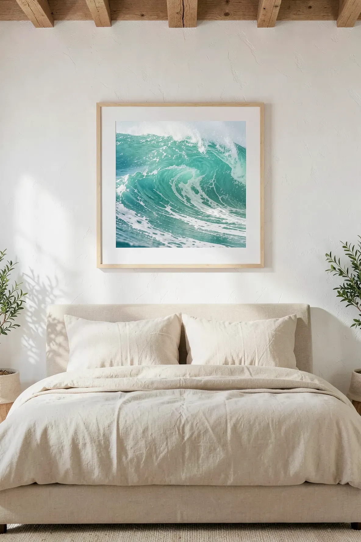 A large framed photograph of a turquoise ocean wave hanging above a bed in a boho room.