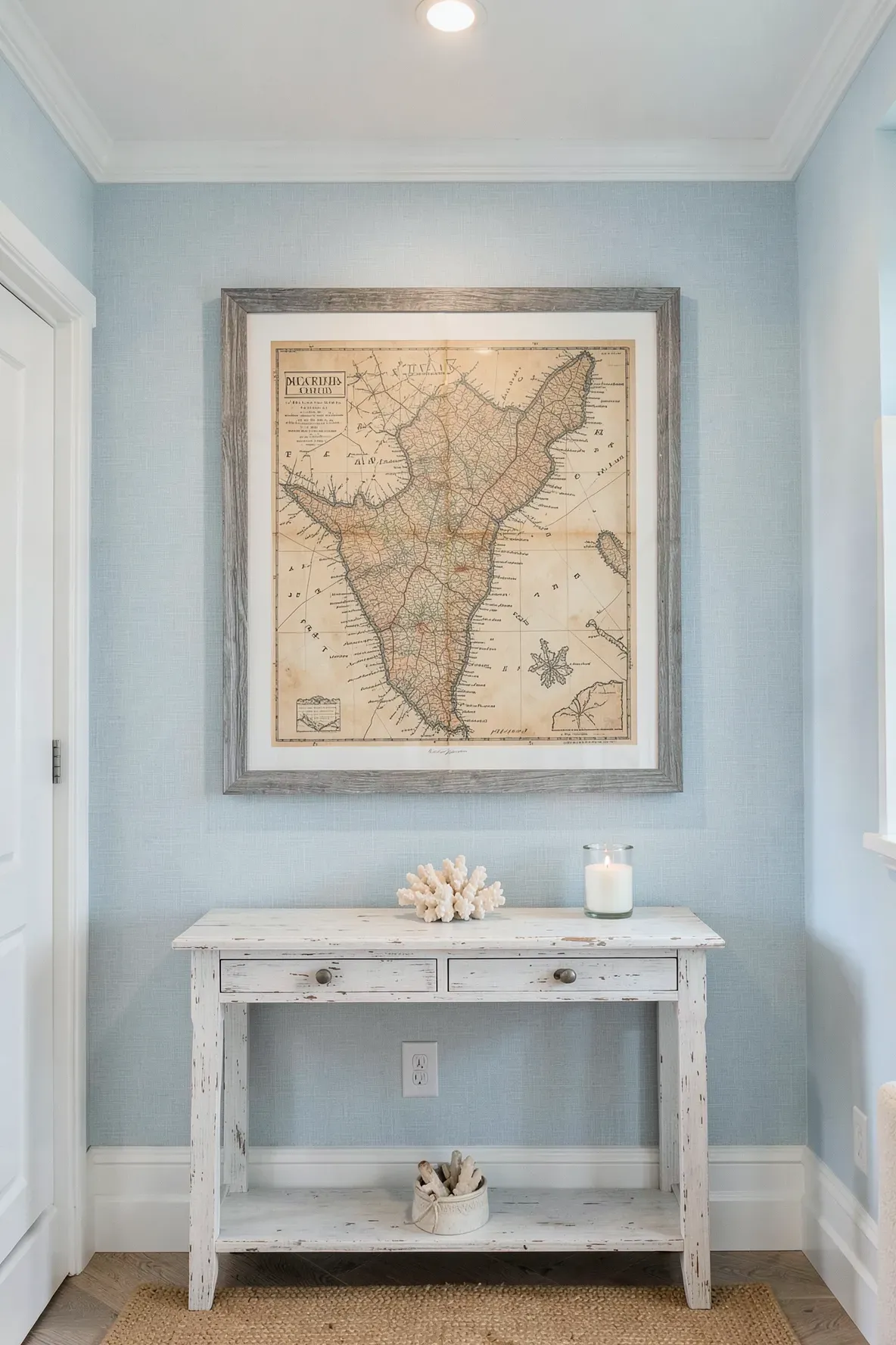 A large vintage coastal map in a gray wood frame hanging above a white console table.