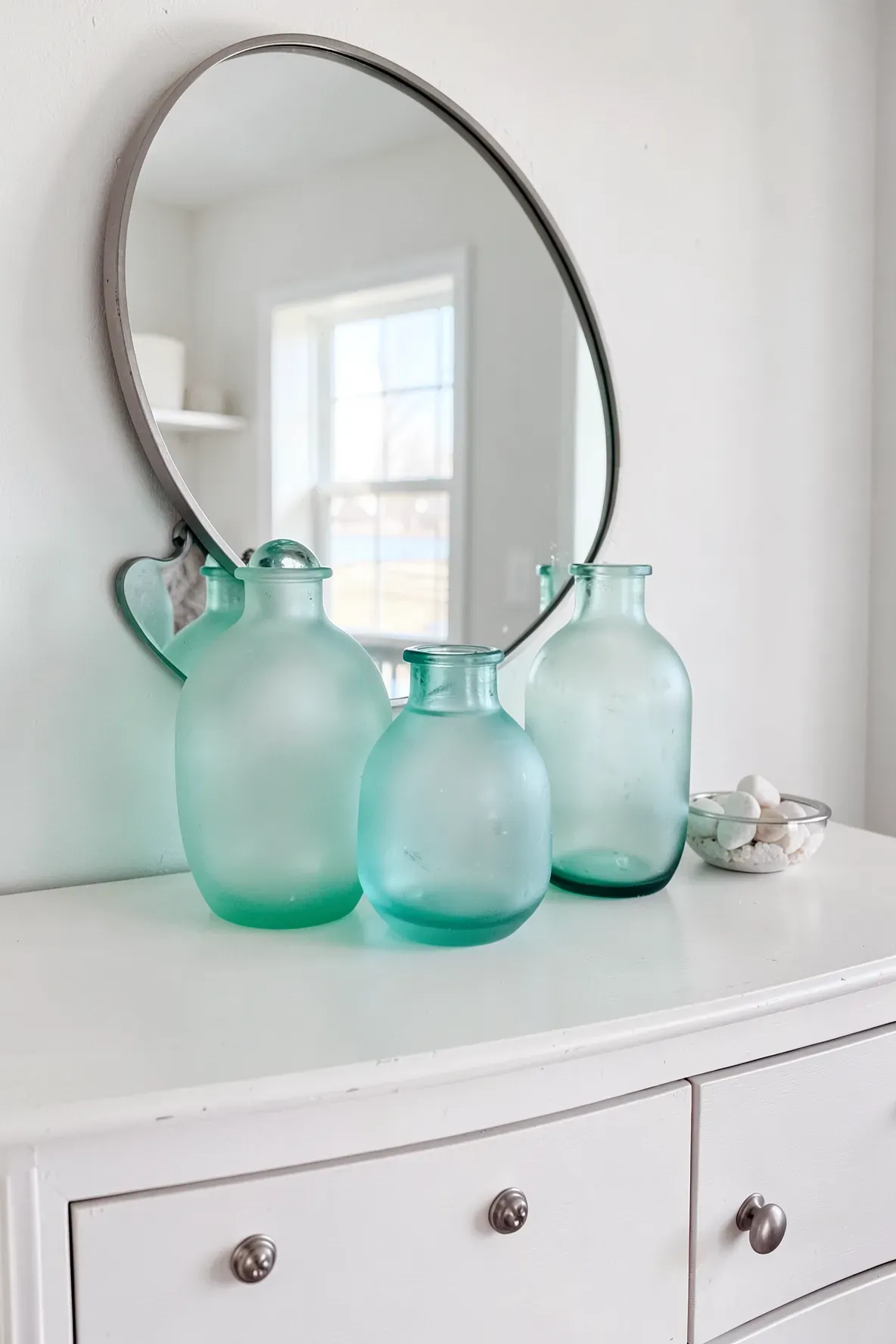 Three frosted glass vases in shades of aqua and teal on a white dresser.