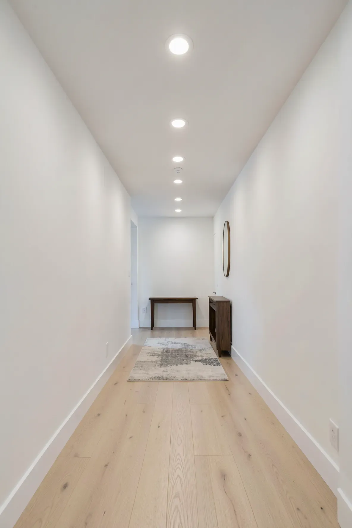 A long narrow hallway with evenly spaced recessed LED lights and light wood floors.