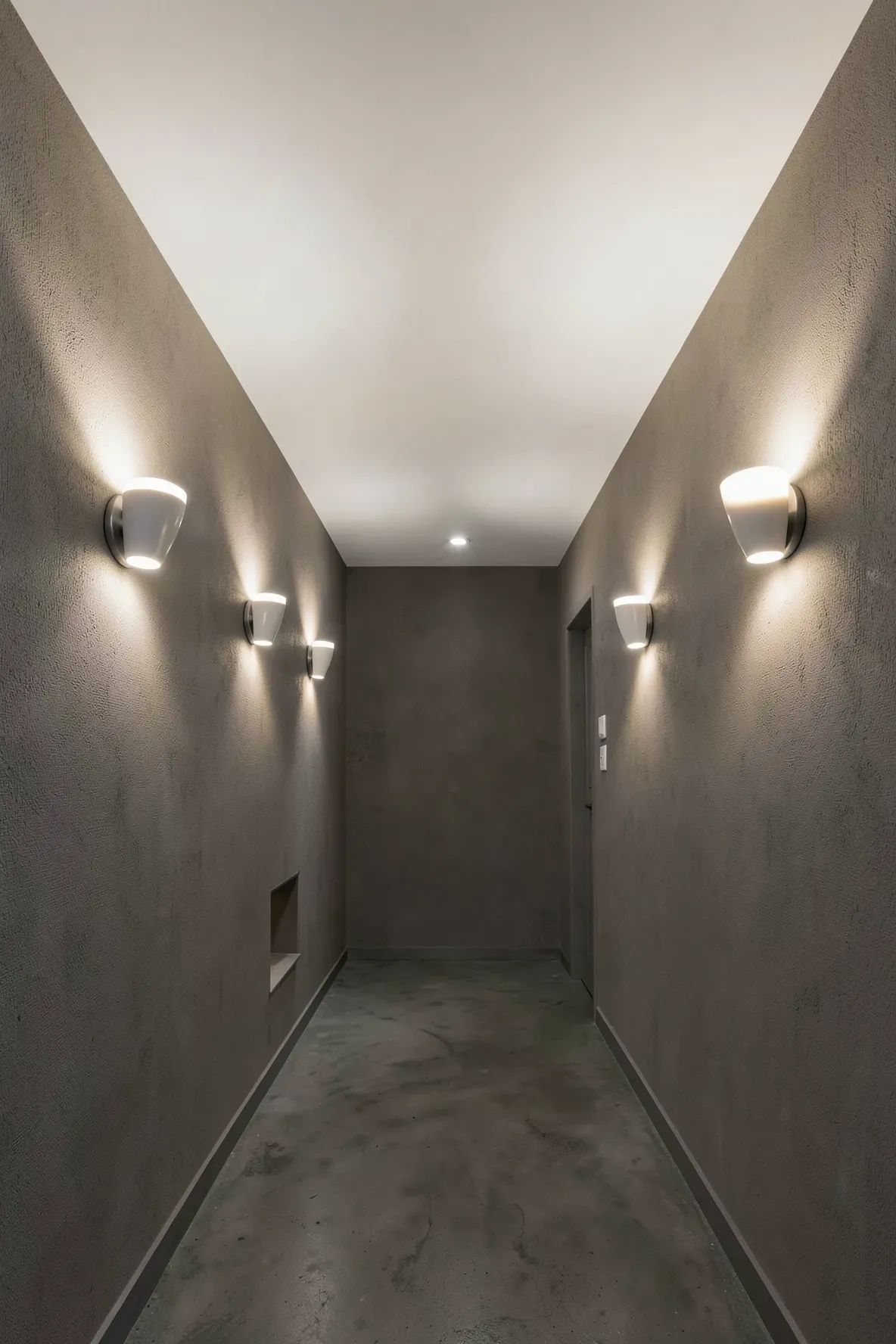 Sleek wall sconces pointing light upward toward the ceiling in a narrow hallway.