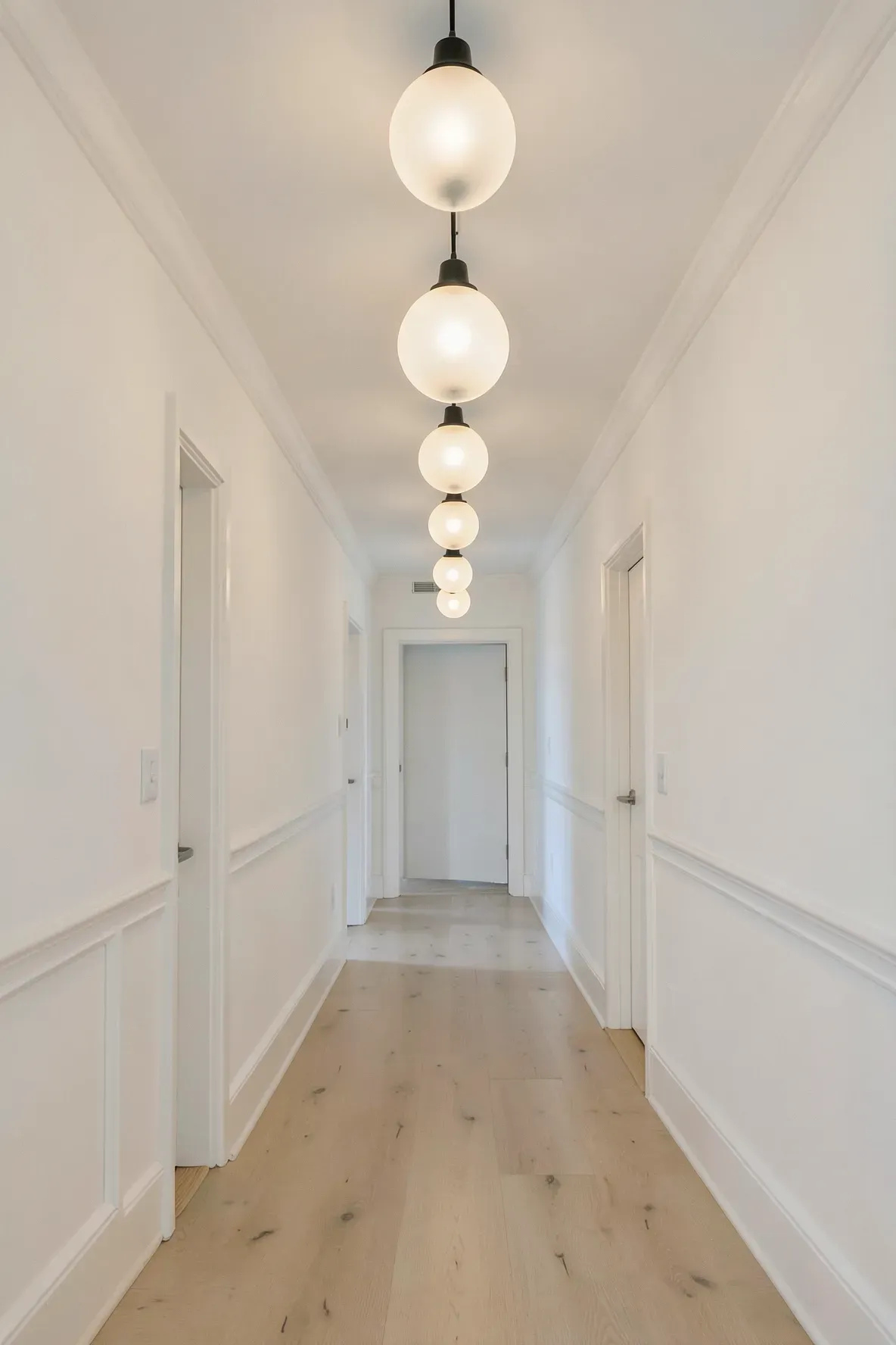 A long narrow hallway illuminated by a series of glowing opal glass globe pendant lights.