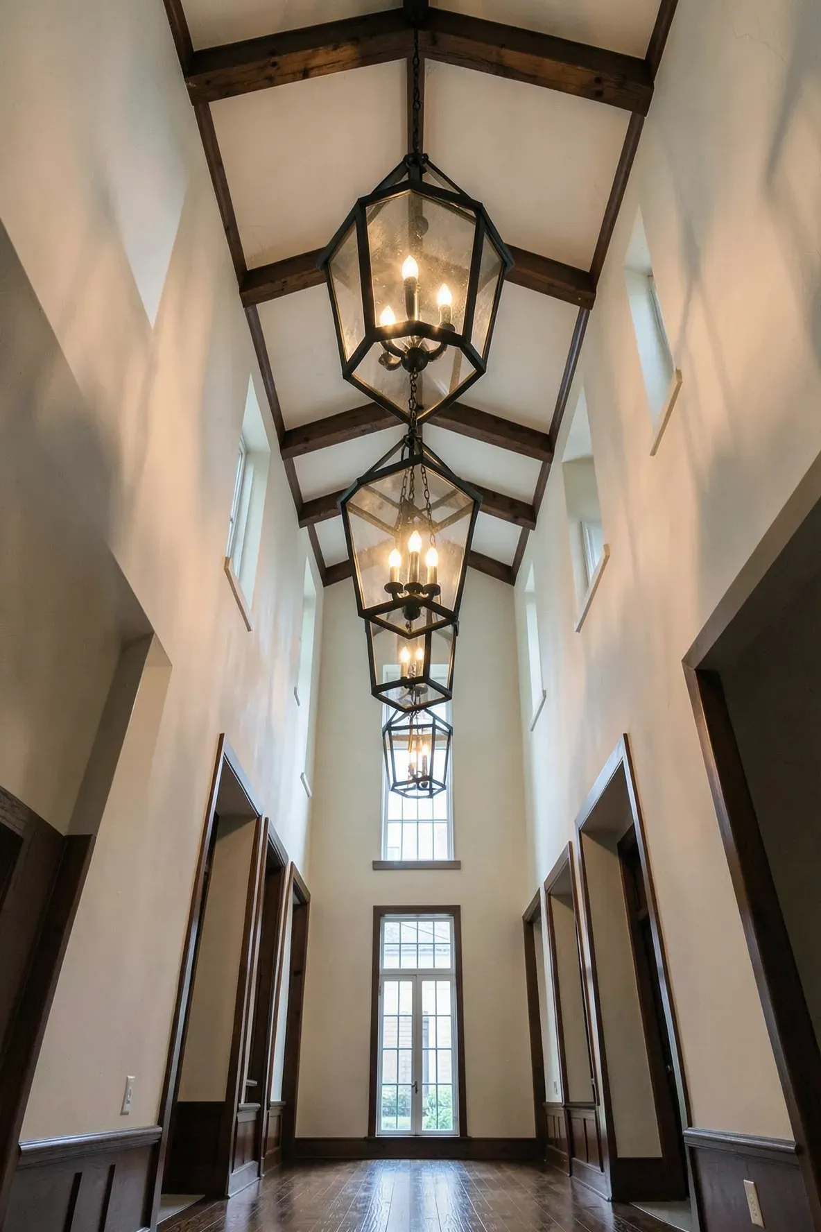 A tall hallway with high ceilings featuring large black open-frame lantern pendant lights.