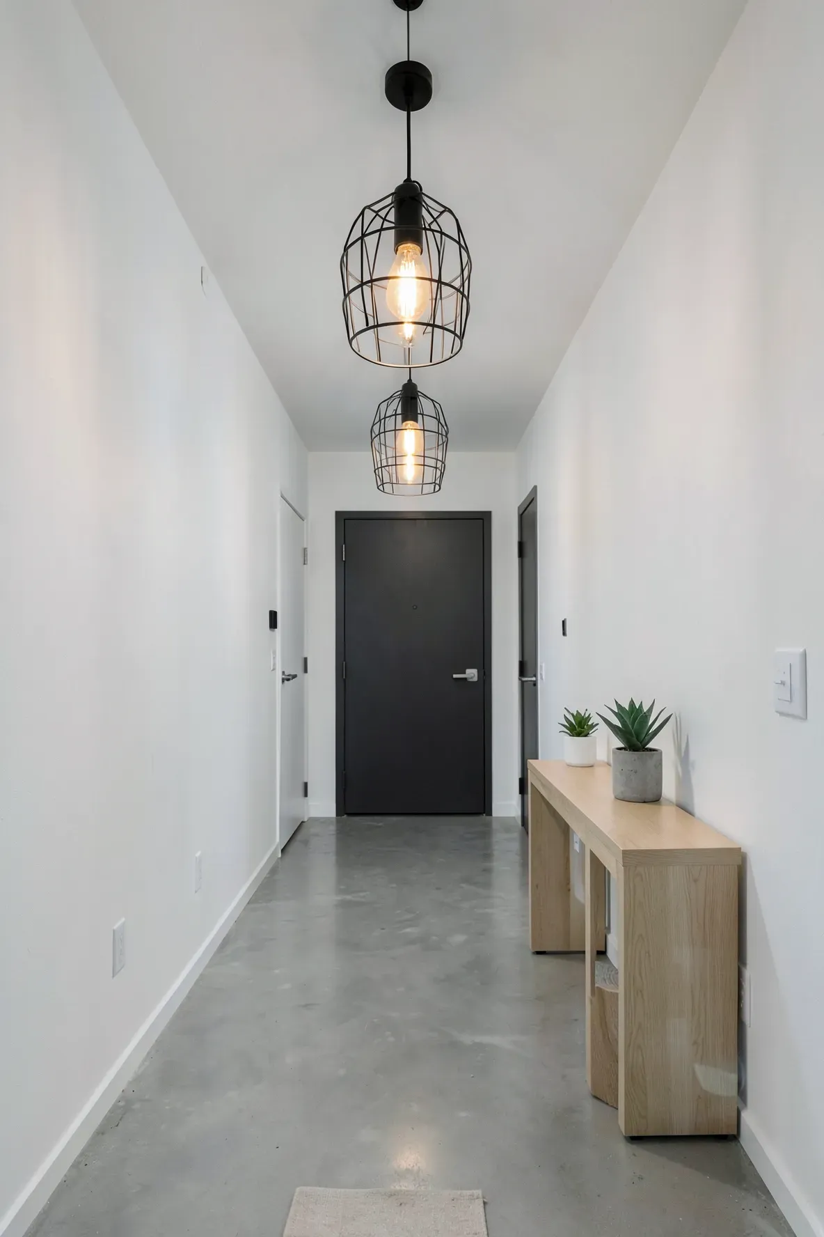 Three black industrial cage pendant lights hanging in a long, modern white hallway.