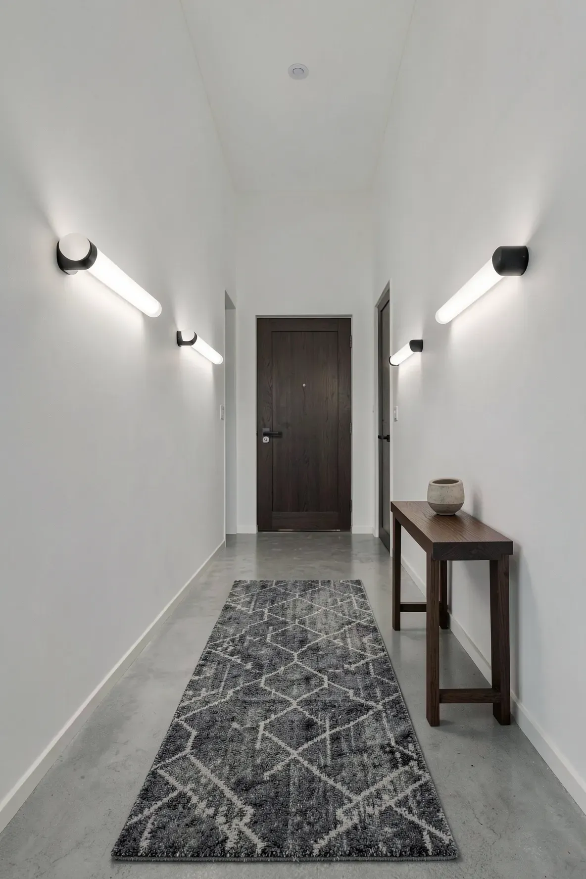 A long narrow hallway illuminated by horizontal frosted glass tube lights on white walls.