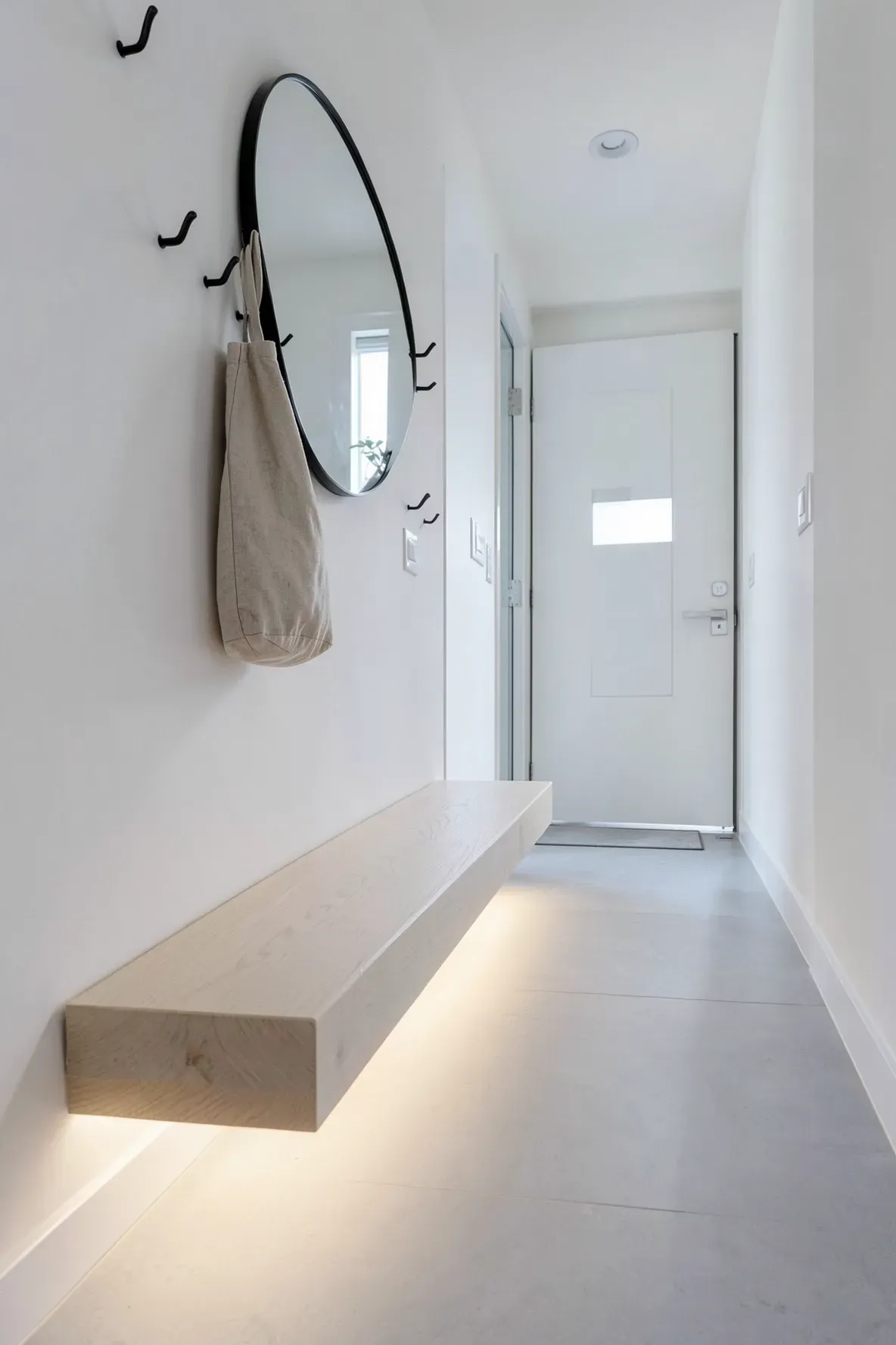 A narrow entryway featuring a floating oak bench with hidden LED lighting underneath glowing on the floor.