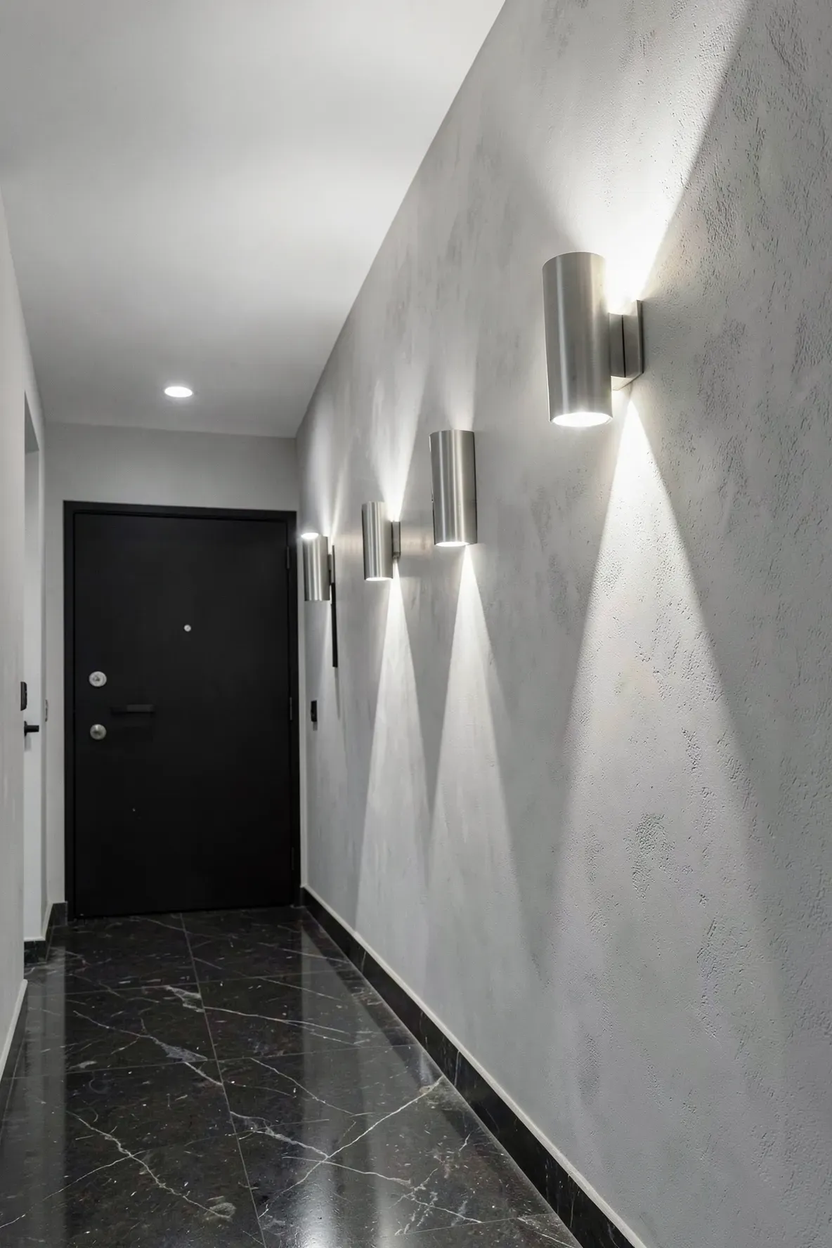 A modern hallway with brushed nickel sconces casting V-shaped light patterns on the walls.