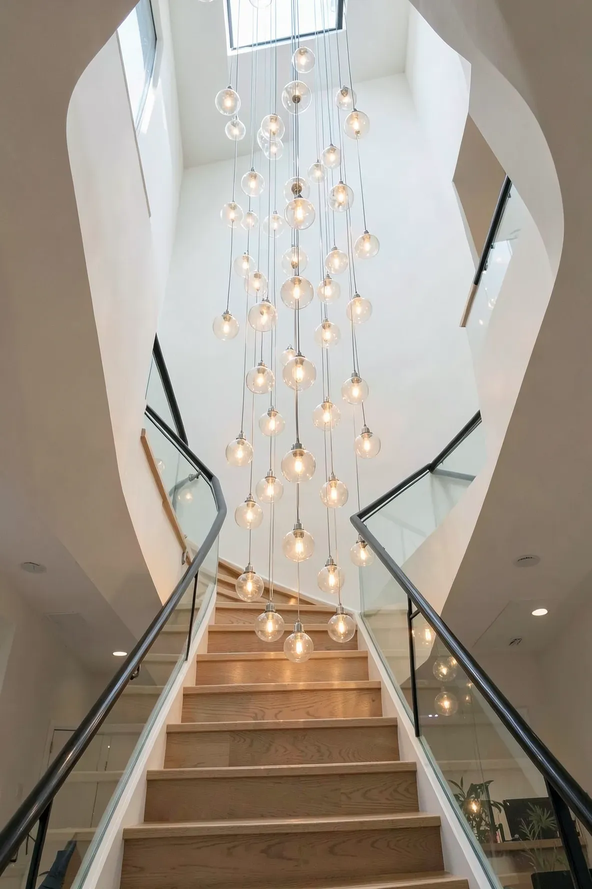 A tall stairwell with a cascading cluster of glass globe pendants hanging at different heights.