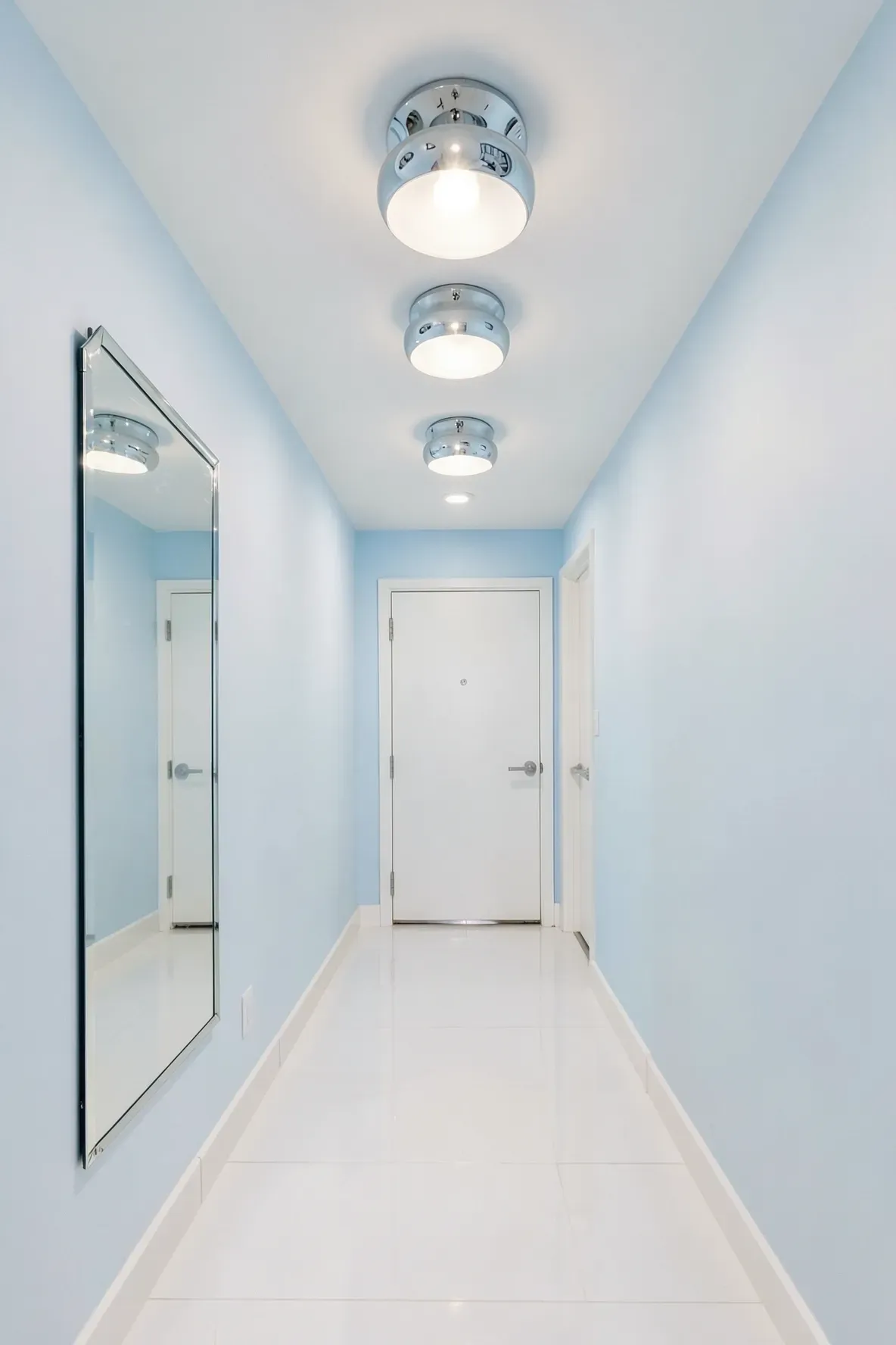 A bright modern hallway with polished chrome ceiling lights and a large wall mirror.