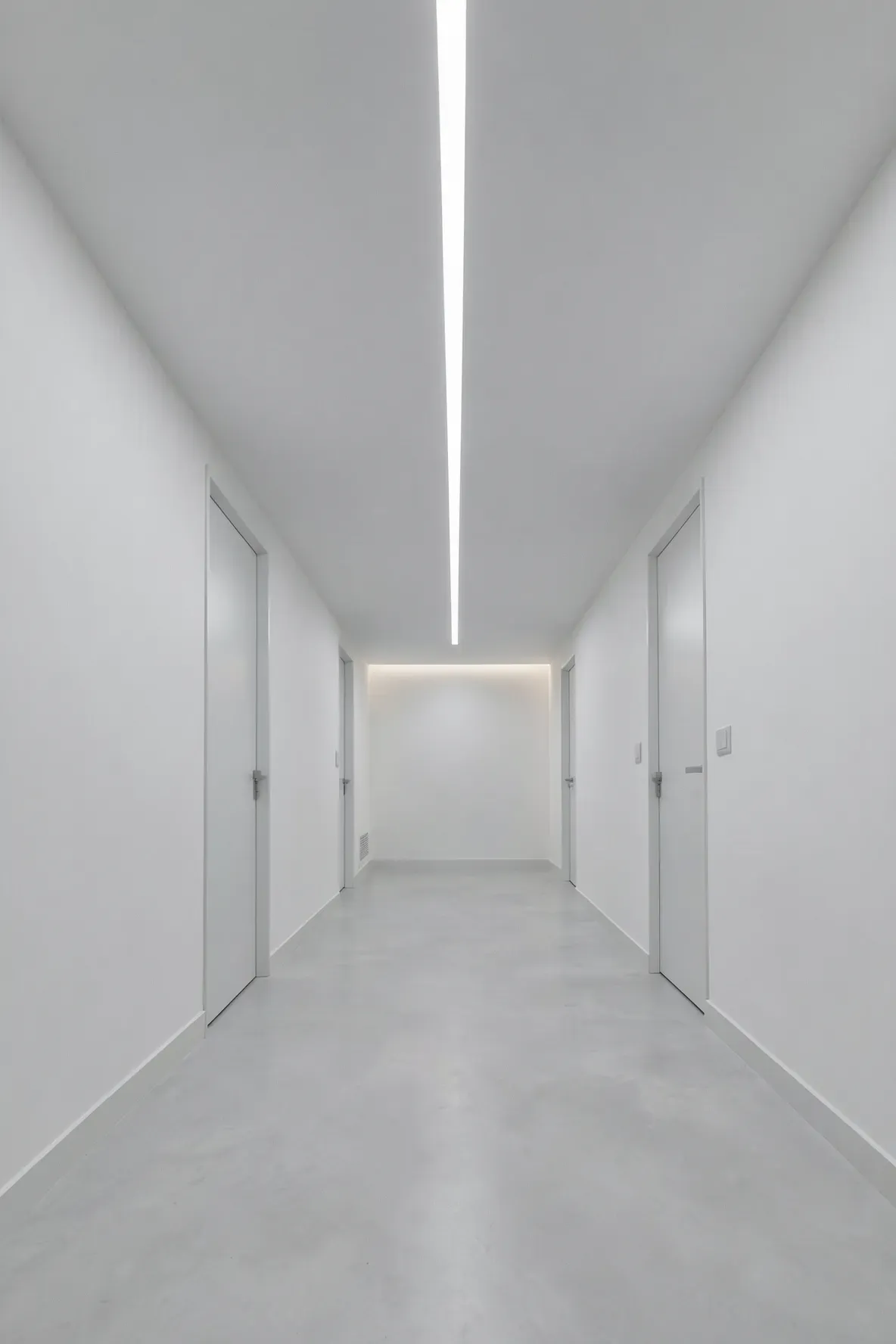 A long minimalist hallway with a single continuous line of recessed light in the ceiling.