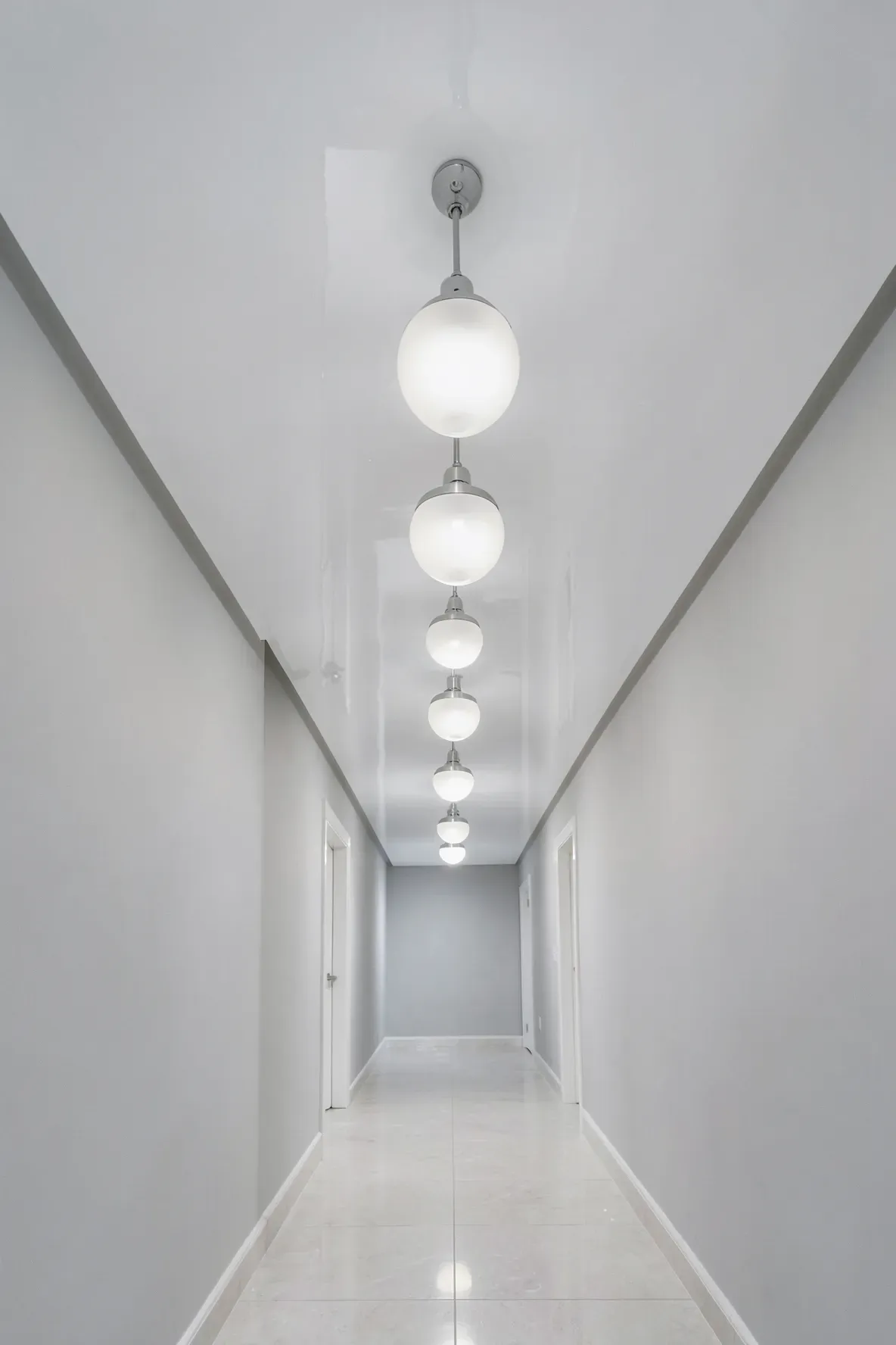 A narrow hallway featuring a shiny high-gloss white ceiling that reflects light and space.