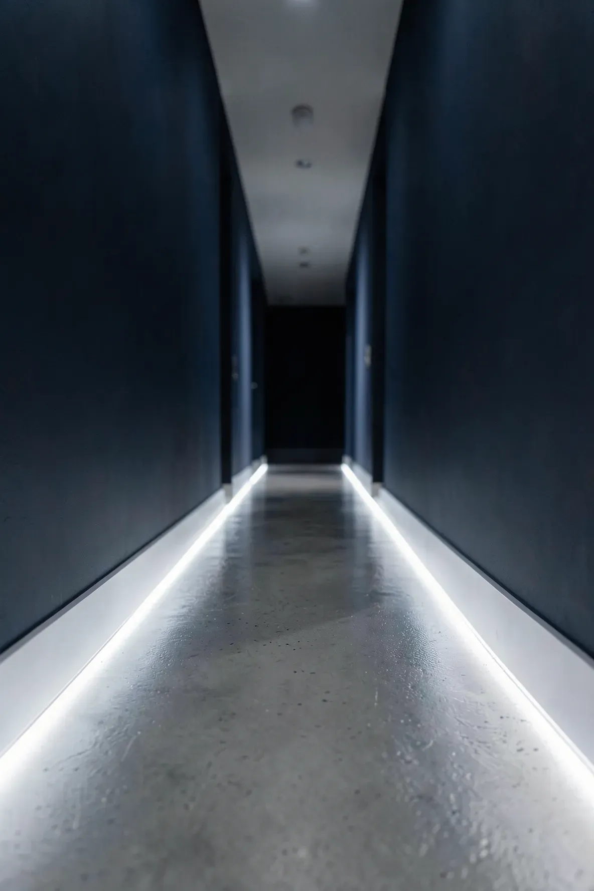 A dark hallway illuminated by glowing LED strips tucked into the baseboards along the floor.
