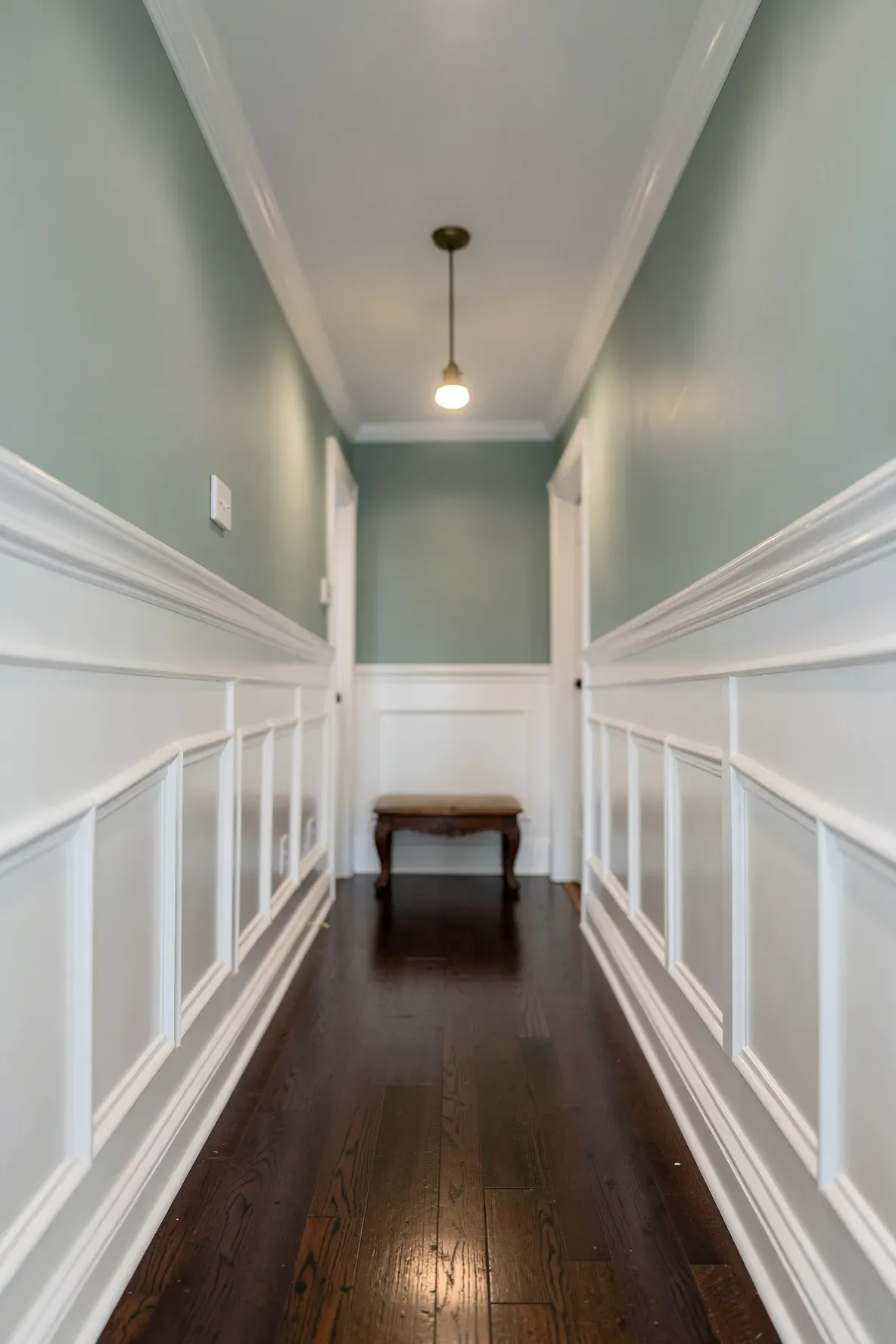 A narrow hallway with white wood paneling on the lower half of the walls and sage green paint above.