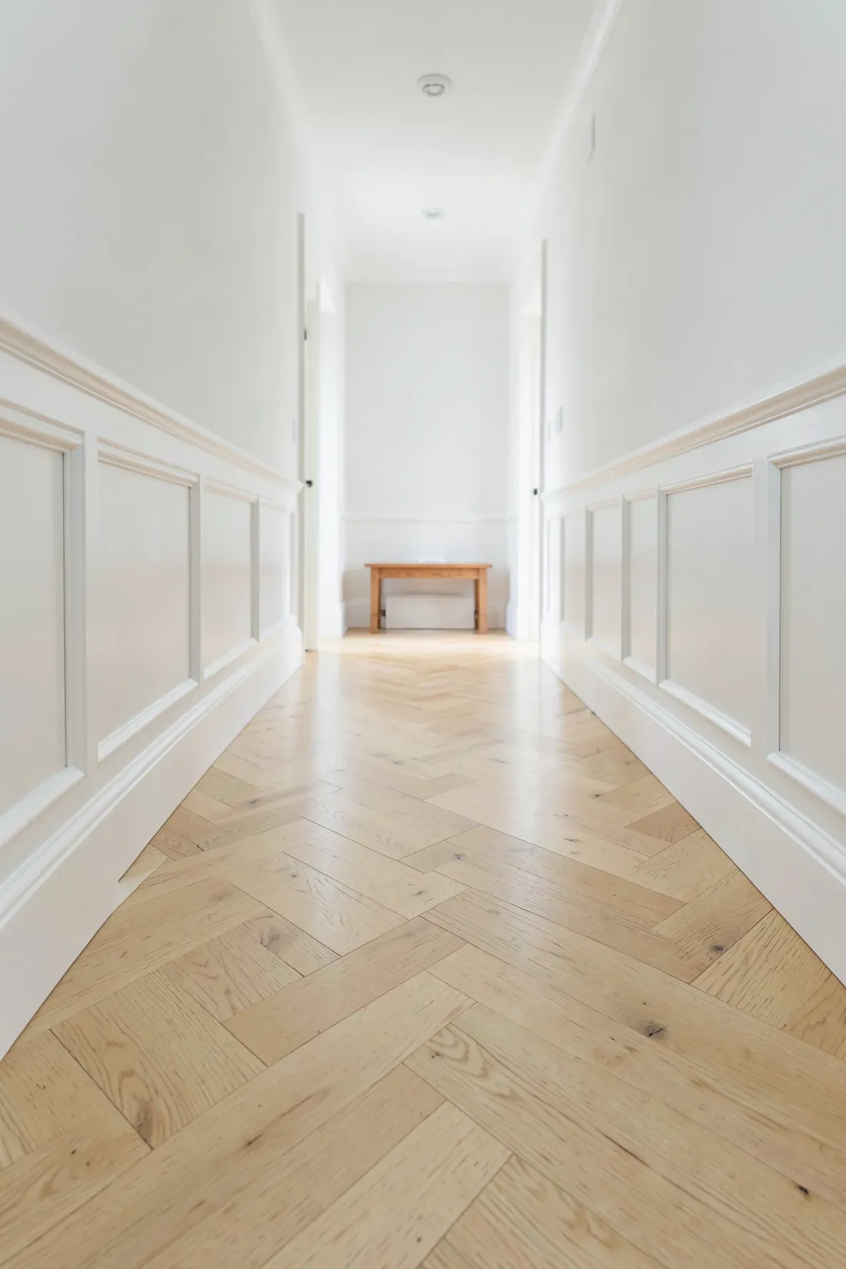 Light oak herringbone wood flooring in a bright, narrow hallway with white walls.