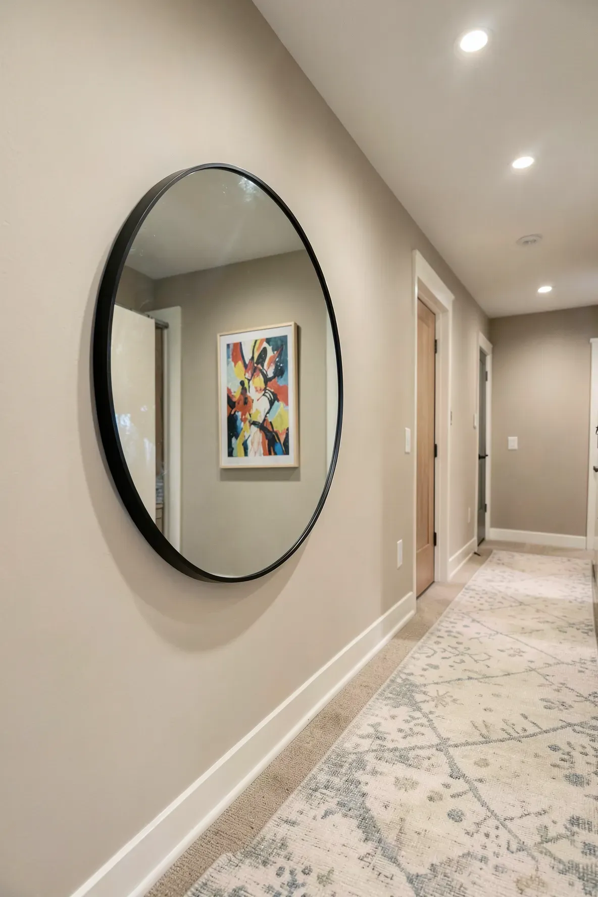 A large round black-framed mirror on a neutral wall in a long hallway.