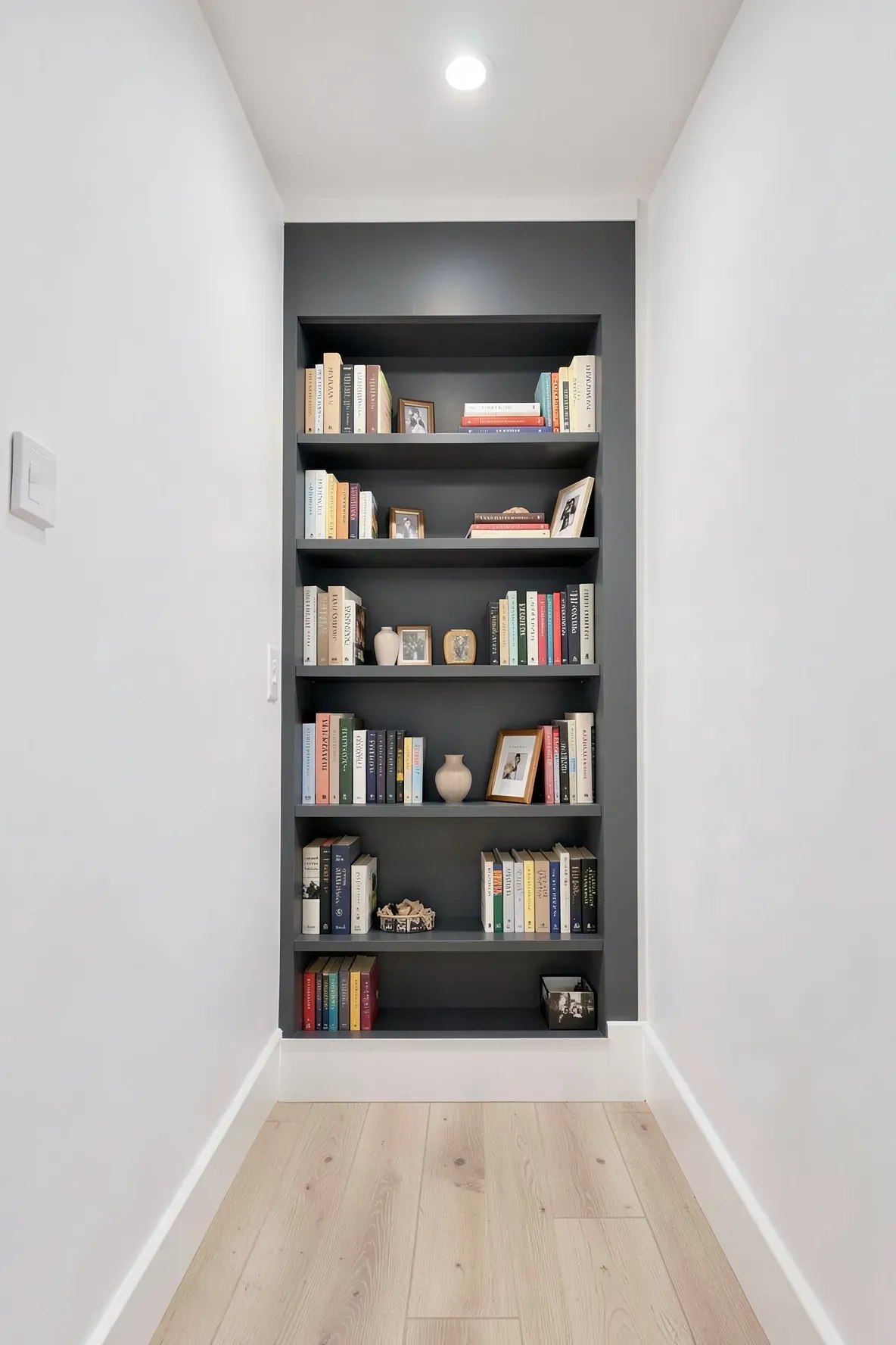 Shallow bookshelves built into a hallway wall, filled with books and decor.