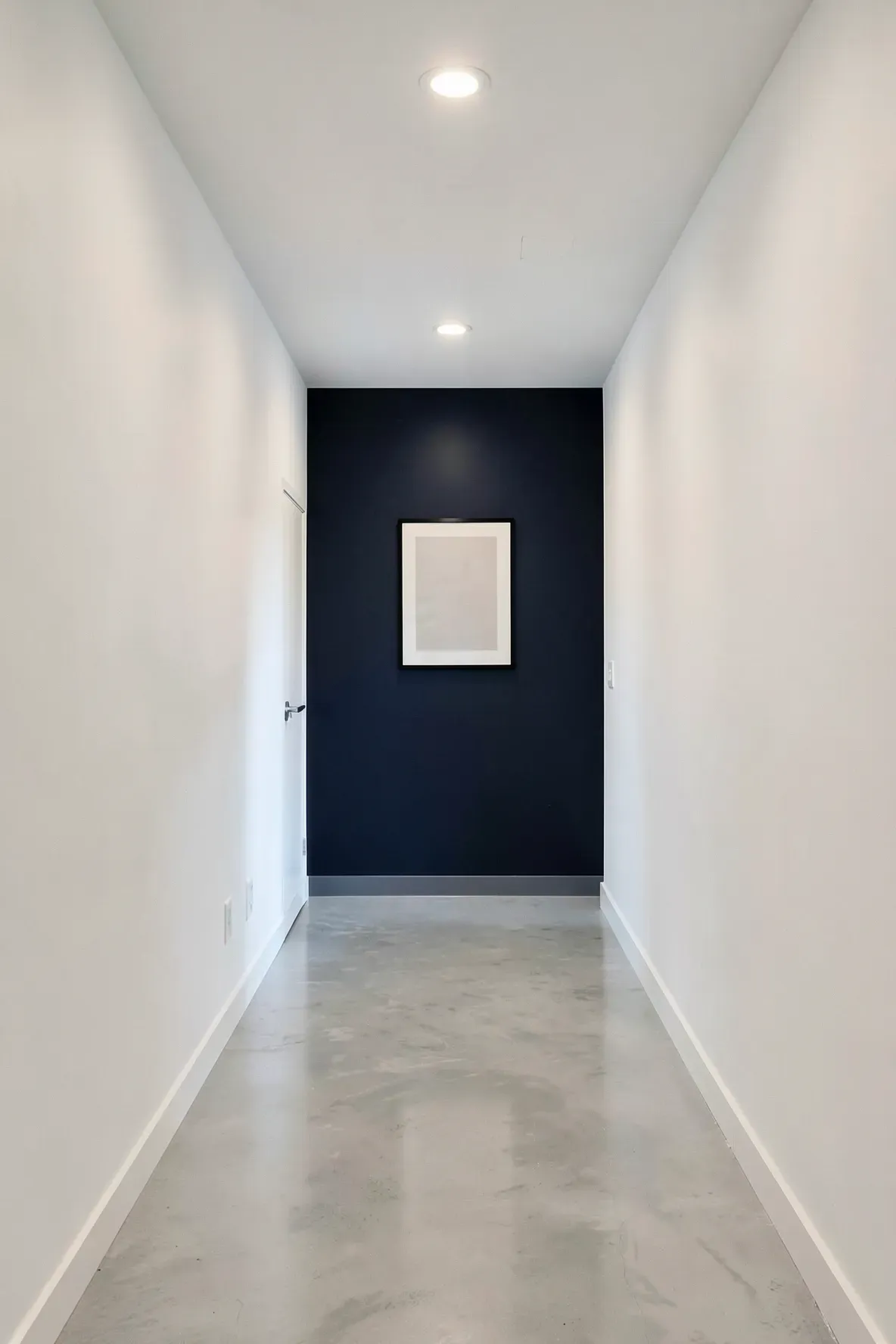 A long hallway with white side walls and a dark navy accent wall at the far end.