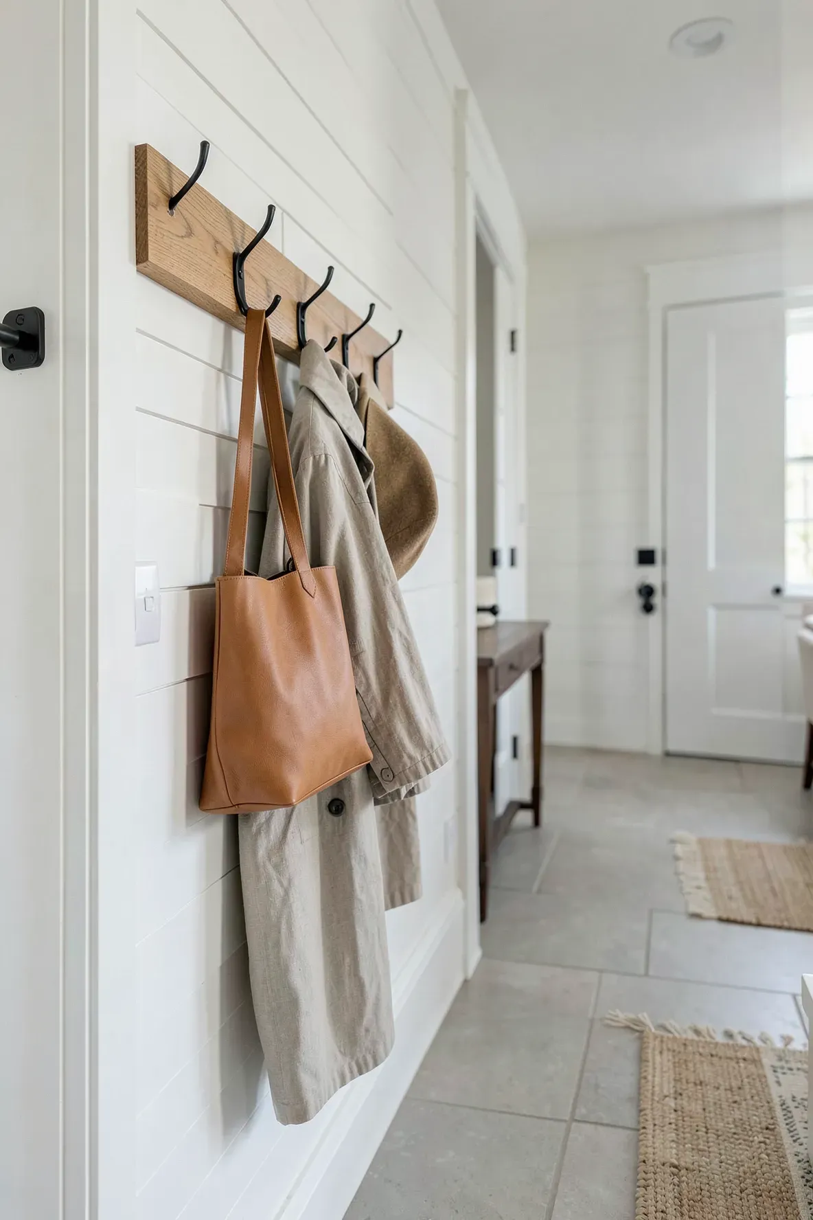 A wooden wall rail with black hooks holding a bag and coat in an organized narrow hallway.