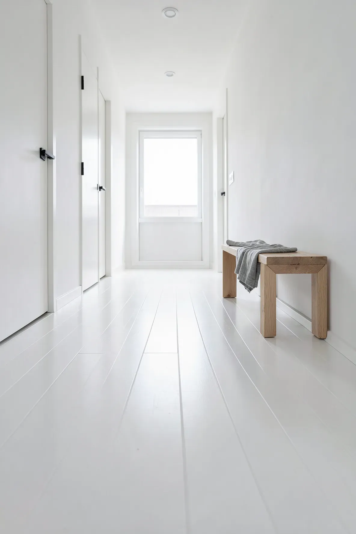 A bright hallway with white painted wooden floors and a minimalist wood bench.