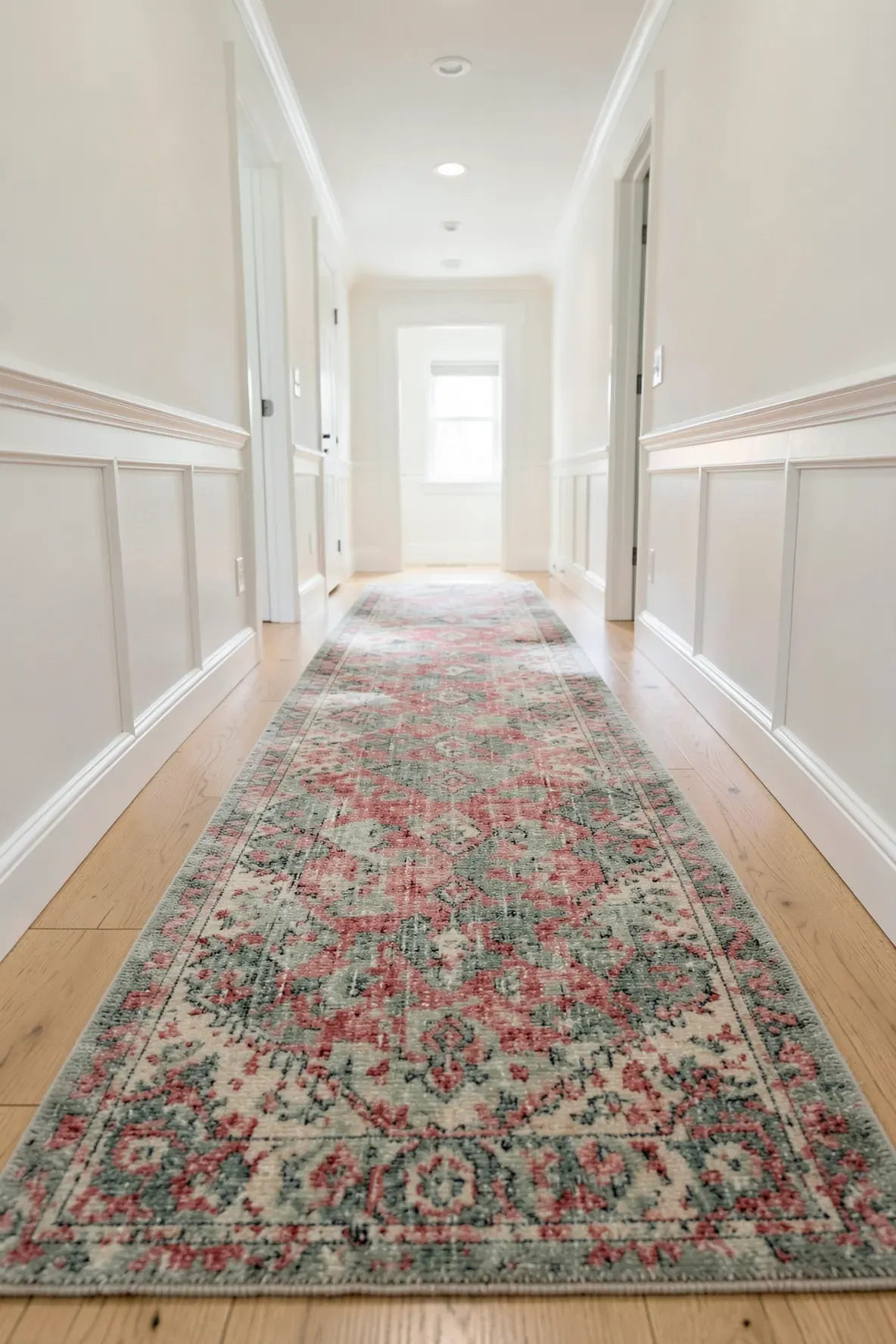 A long vintage runner rug with faded red and blue patterns in a bright farmhouse hallway.