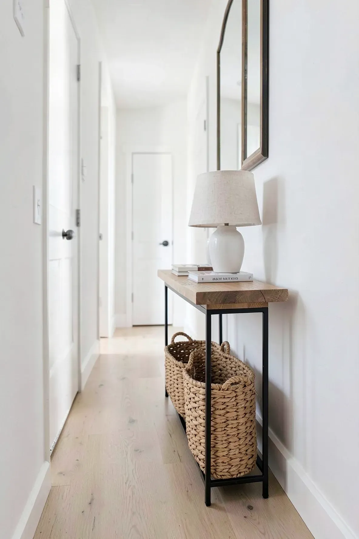 A very thin wood and metal console table with a basket underneath in a narrow hallway.