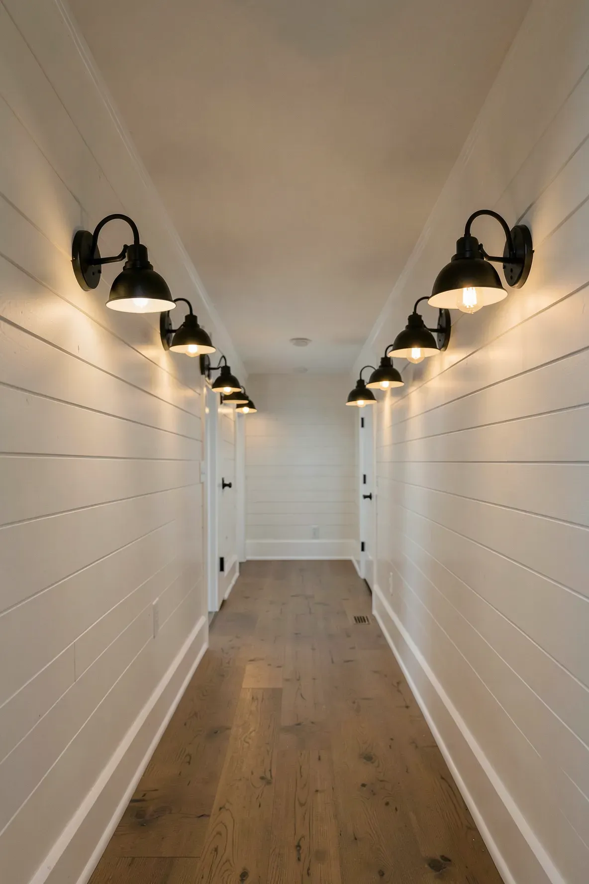 Black metal gooseneck sconces spaced evenly along a white shiplap hallway wall.