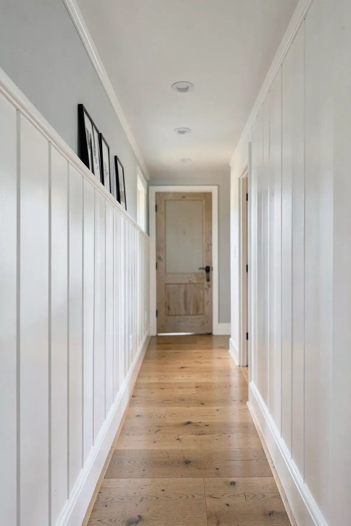 A long narrow hallway with white board and batten paneling and light wood floors.