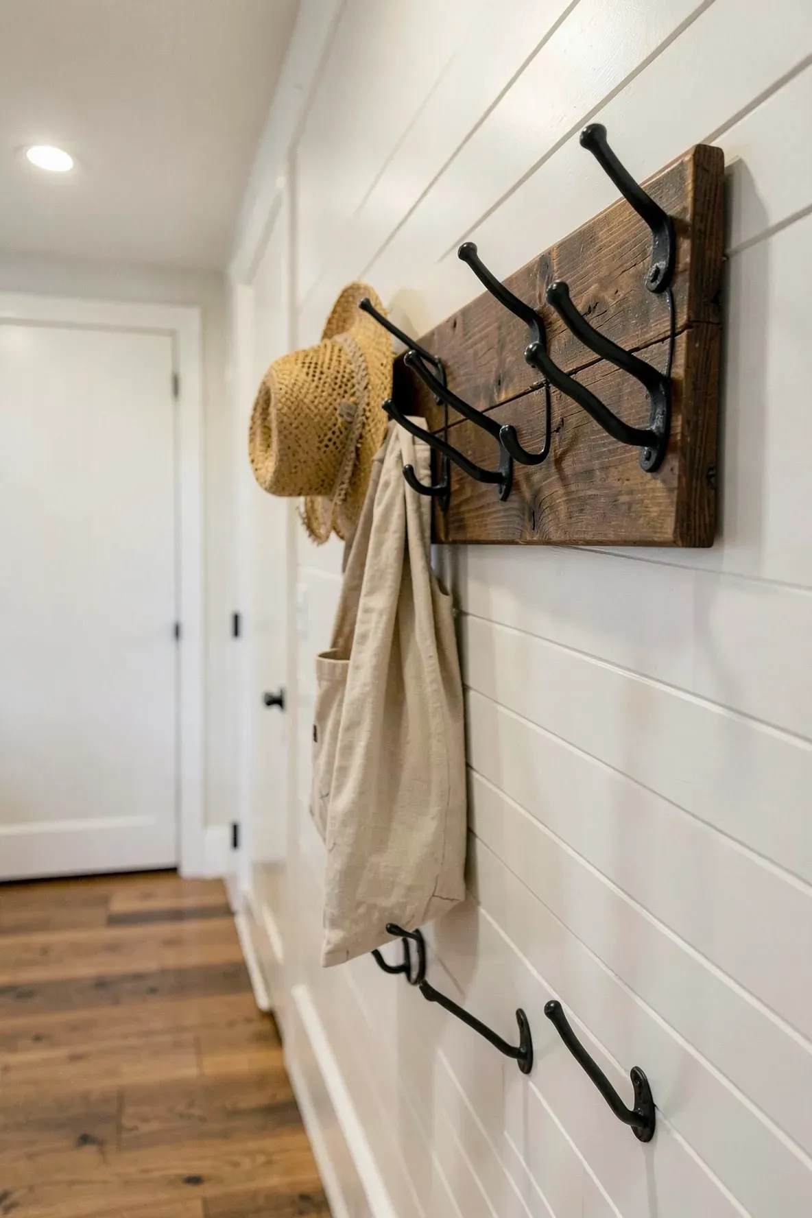 Black iron coat hooks mounted on a dark wood board in a farmhouse hallway.