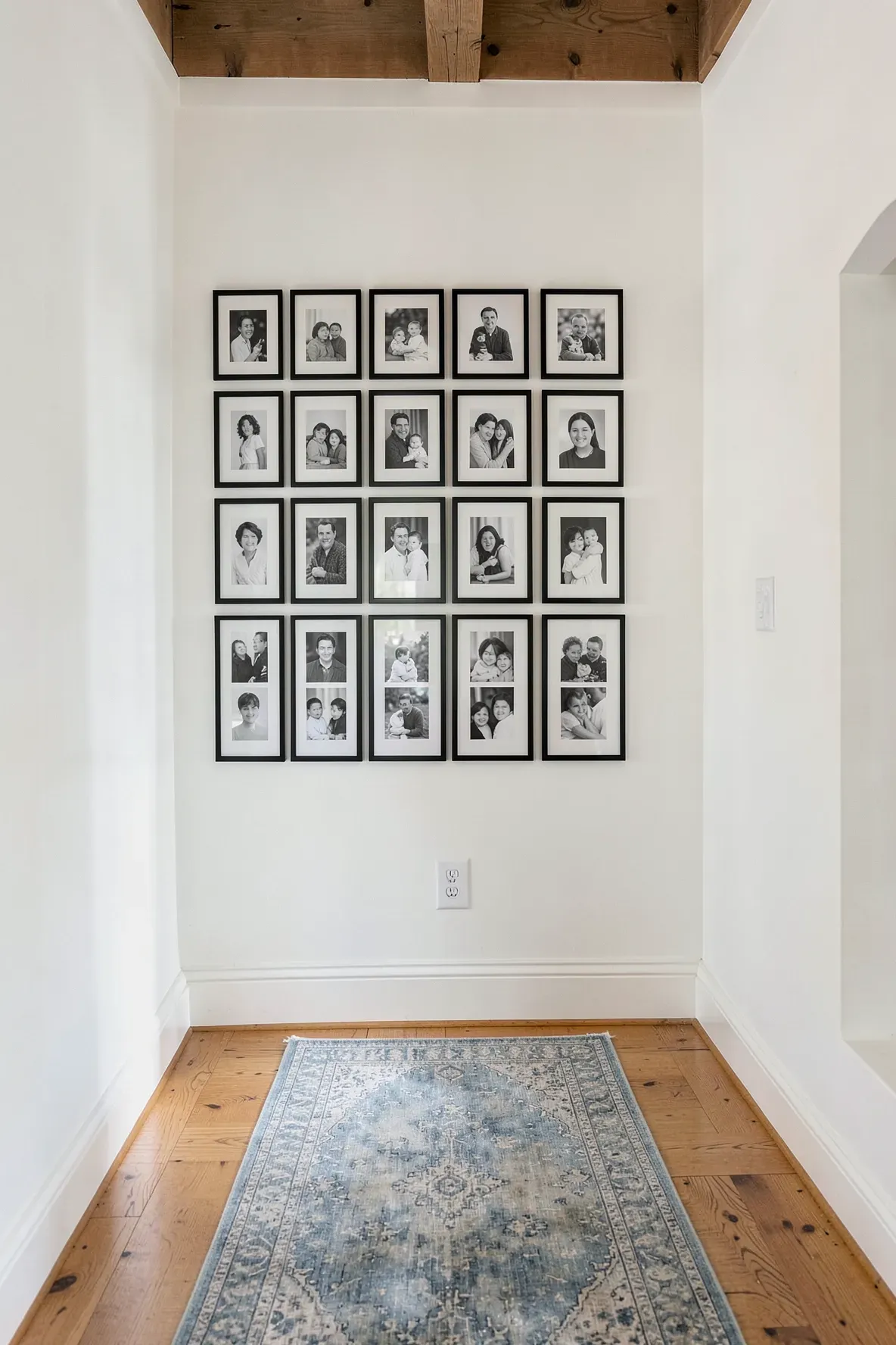A symmetrical grid of black and white family photos in black frames on a hallway wall.