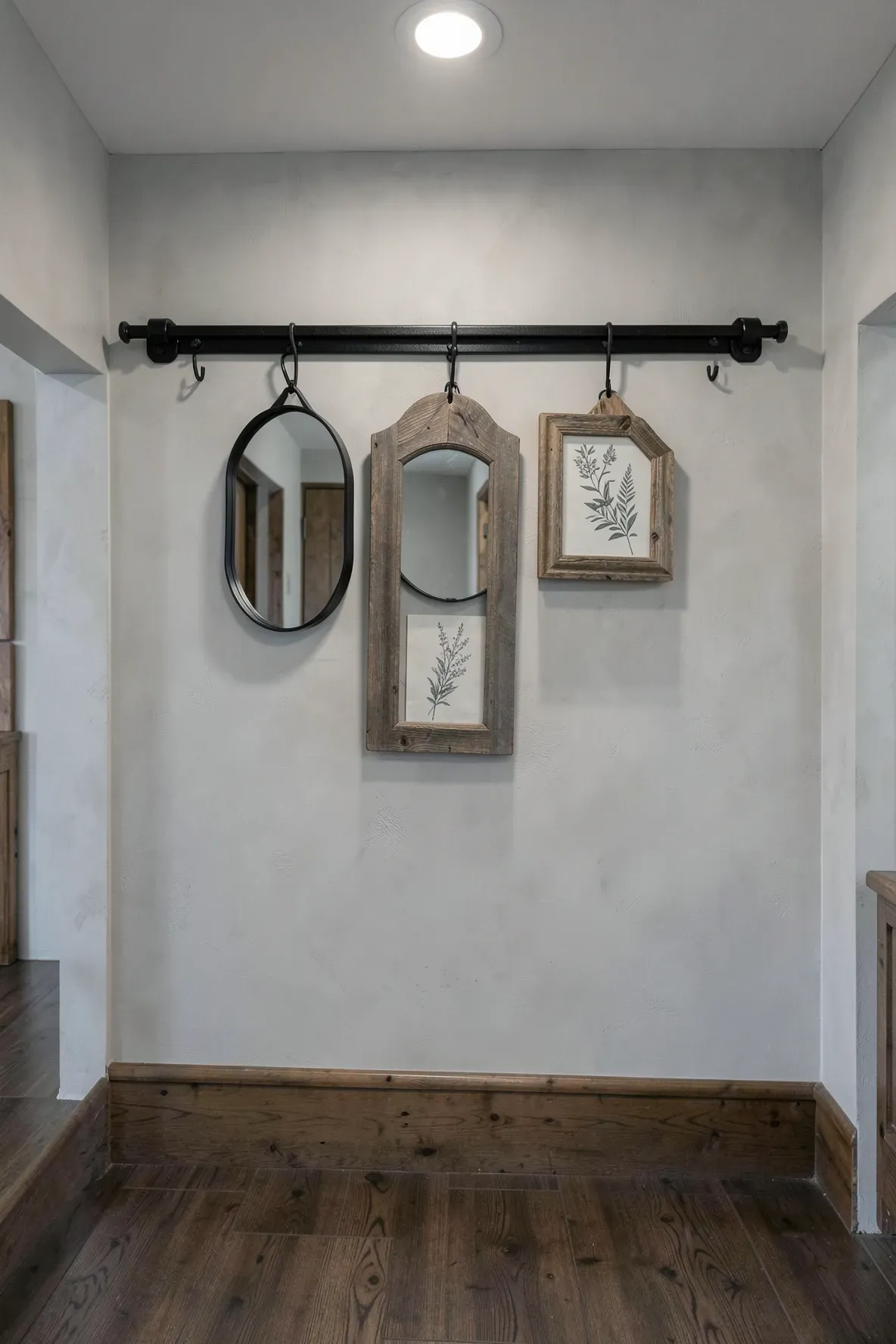 A black industrial barn door track on a hallway wall hanging a mirror and wooden frames.