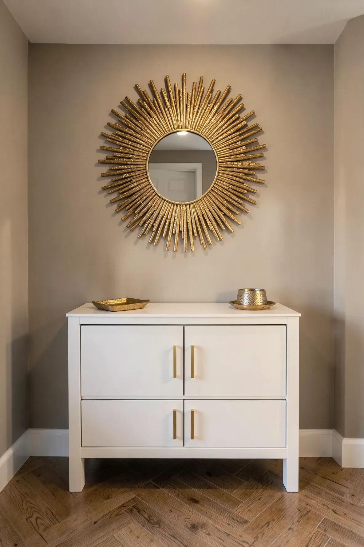 A gold sunburst mirror hanging above a neat white shoe storage cabinet in a warm entryway.