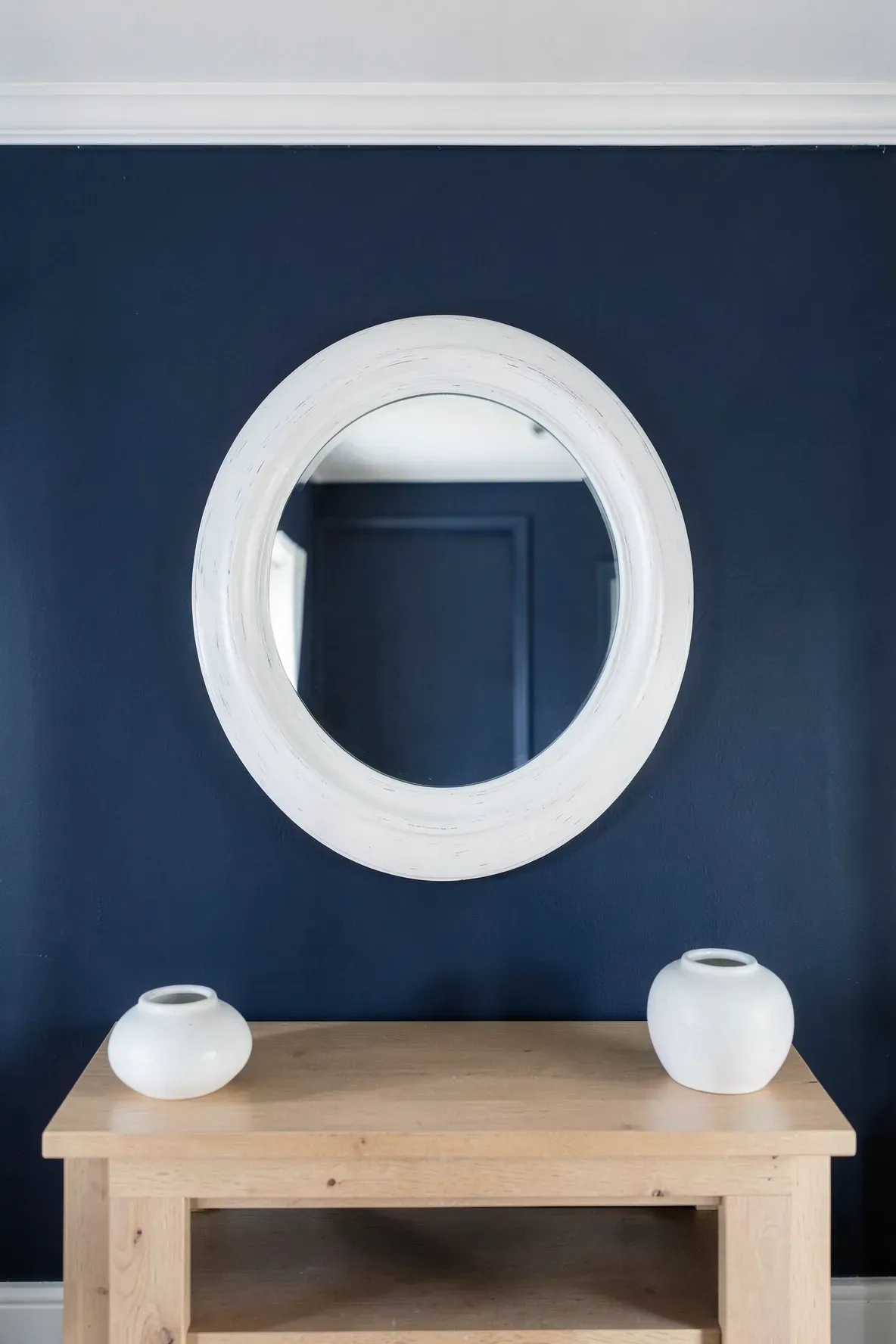 A large round mirror with a thick white frame mounted on a dark navy blue accent wall.