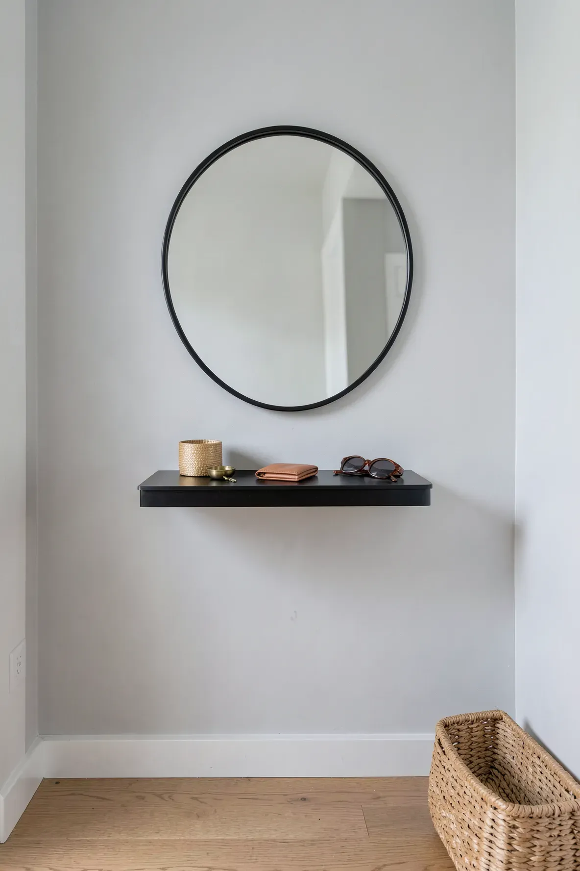 A minimalist black round mirror with a matching floating shelf holding keys and sunglasses.