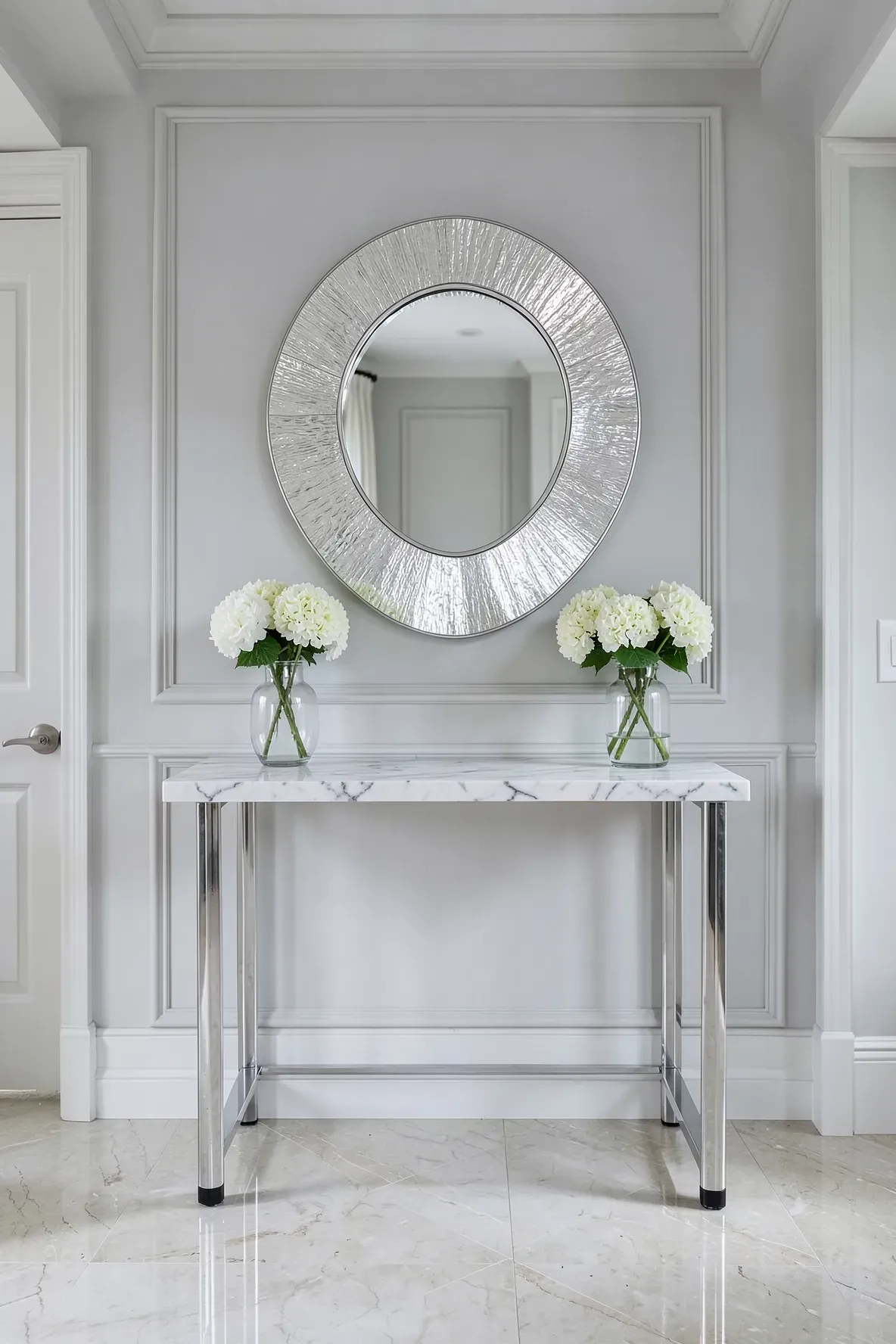 An elegant silver leaf round mirror hanging above a white marble-topped entryway table.