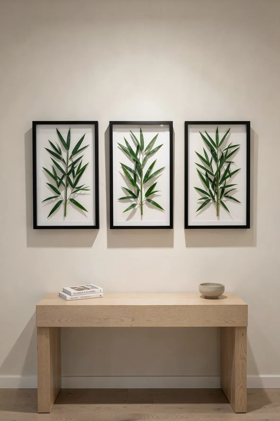 Three black shadow boxes with green bamboo leaves hanging above an oak console table.
