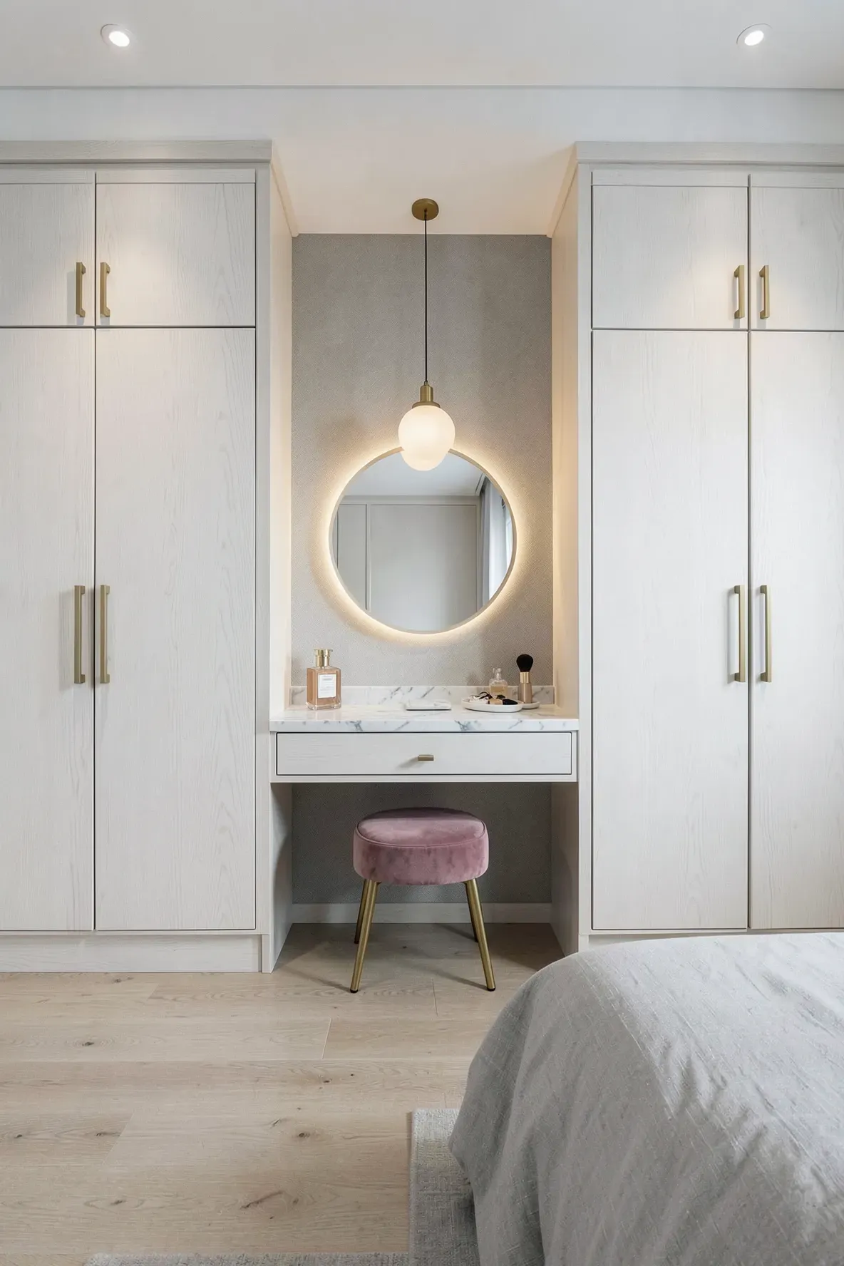 A modern white oak built-in vanity desk with a marble top nestled between two tall wardrobes.