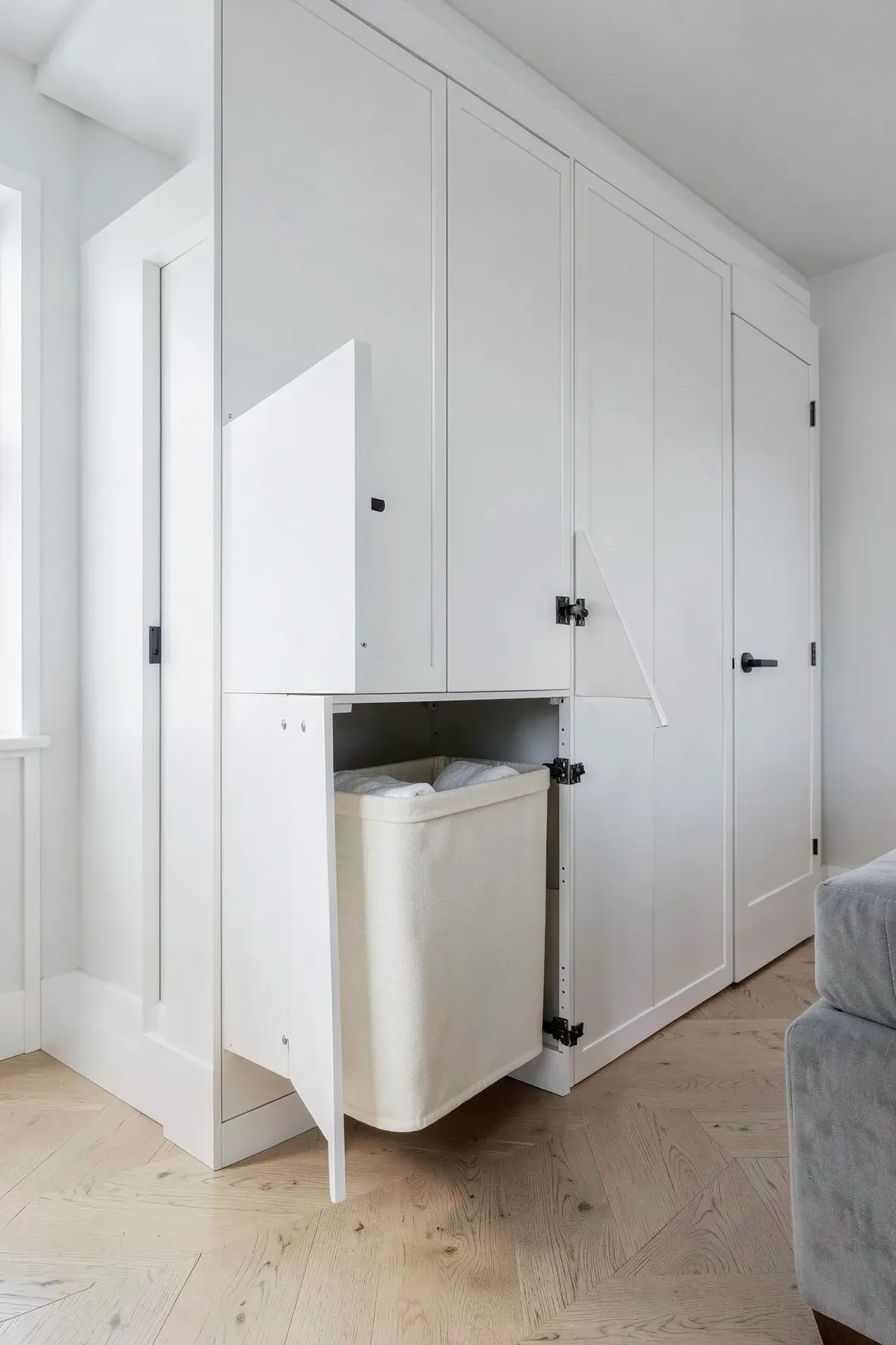 A white built-in bedroom closet with a tilt-out laundry hamper drawer revealing a canvas liner.