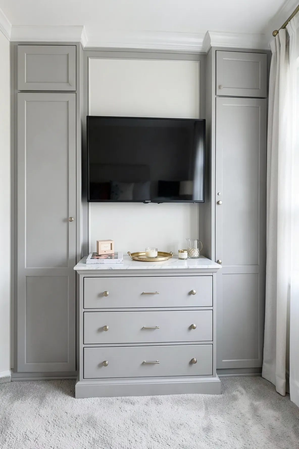 A light gray built-in dresser with a marble top and a flat-screen TV mounted on the wall above it.
