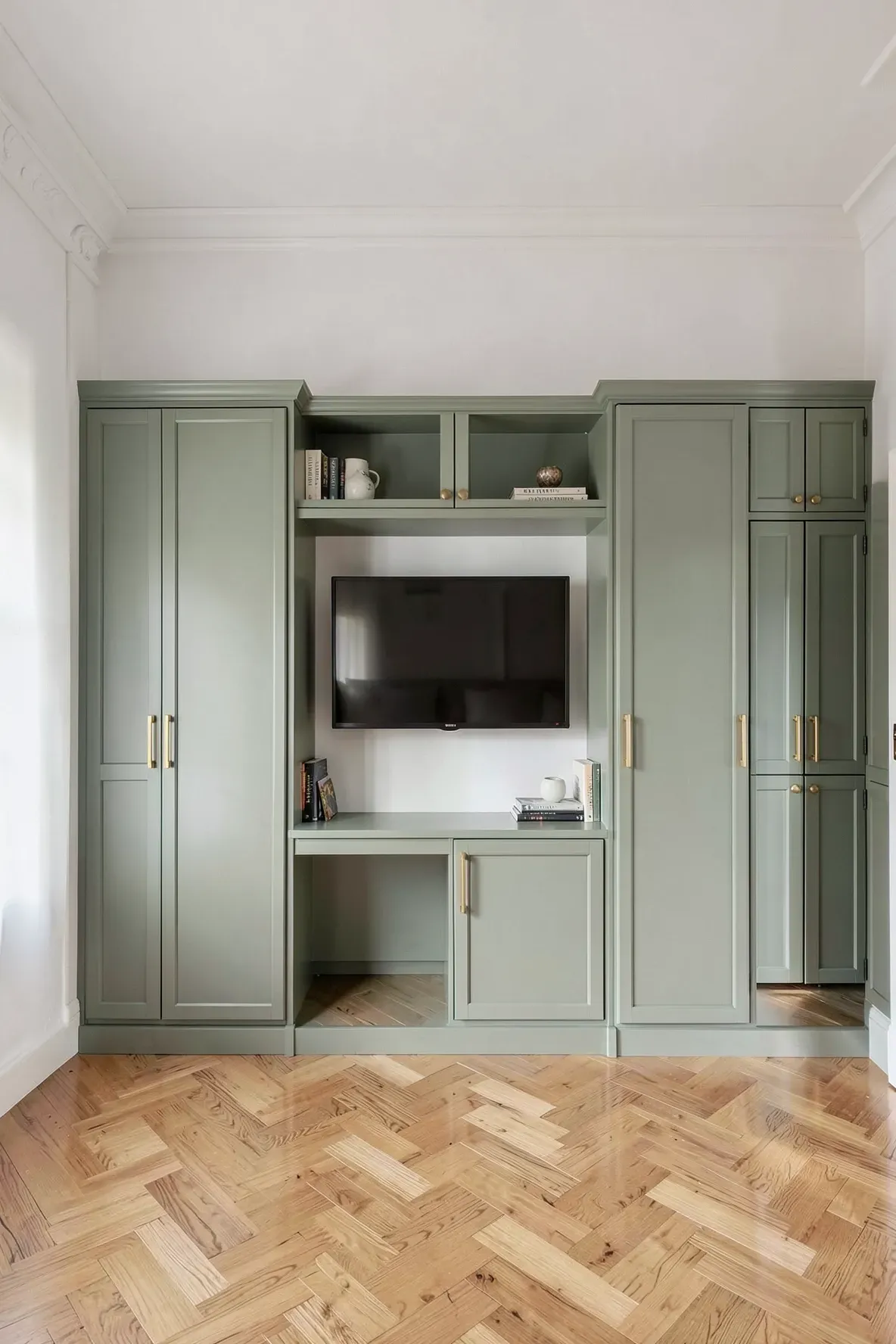 A sage green built-in wardrobe unit with a central media bridge and TV in a bedroom.
