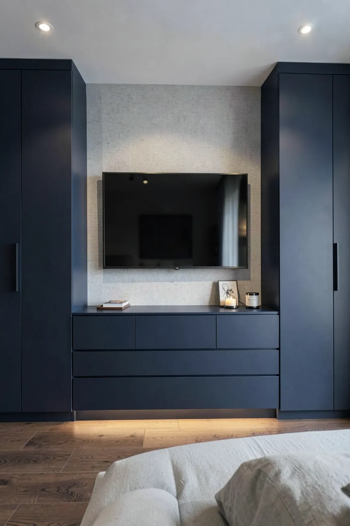 Sleek navy blue low-profile drawers built into a wardrobe wall underneath a mounted TV.