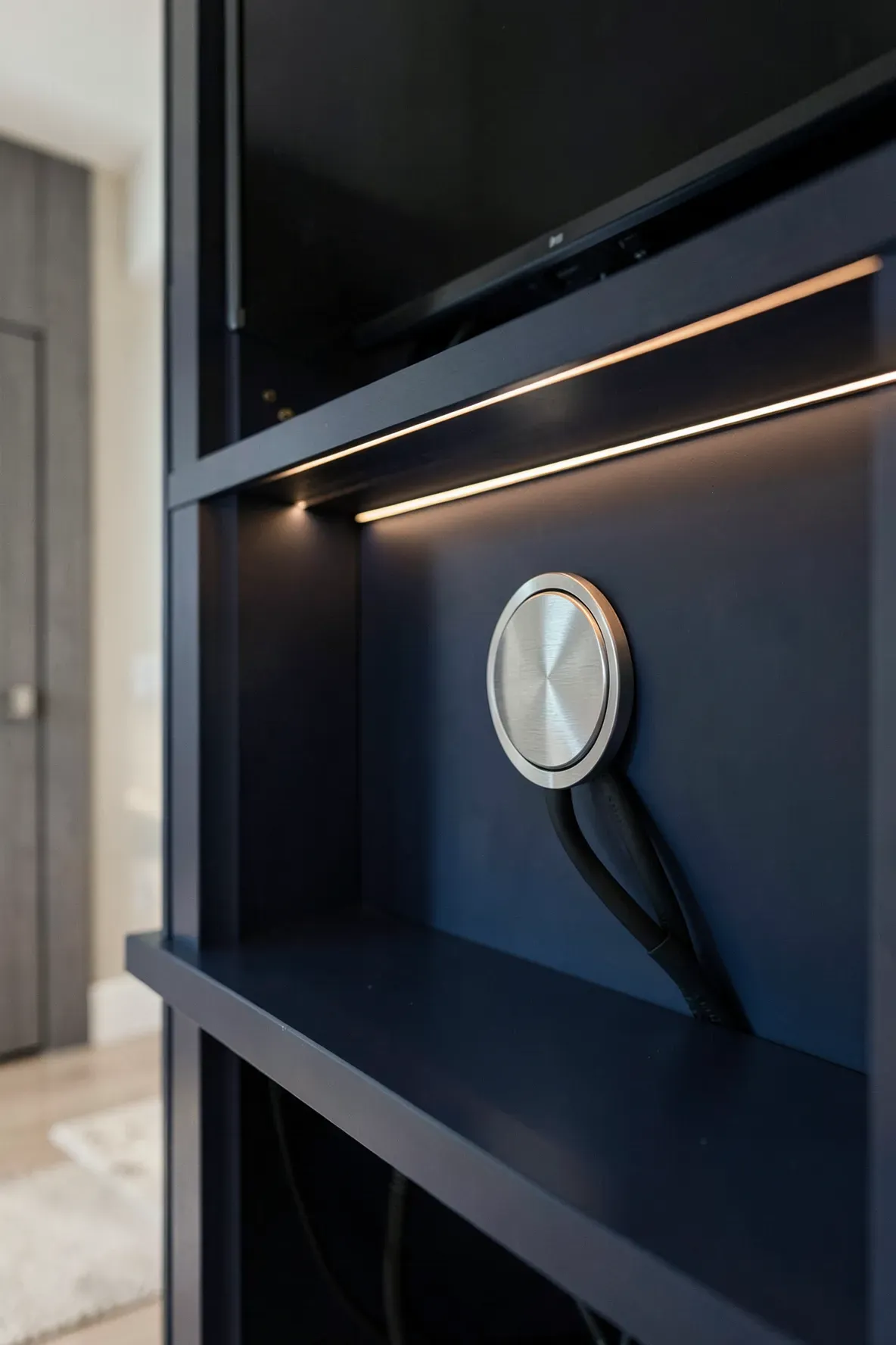 A close-up of a brushed metal cable grommet in a navy blue built-in wardrobe for a TV.